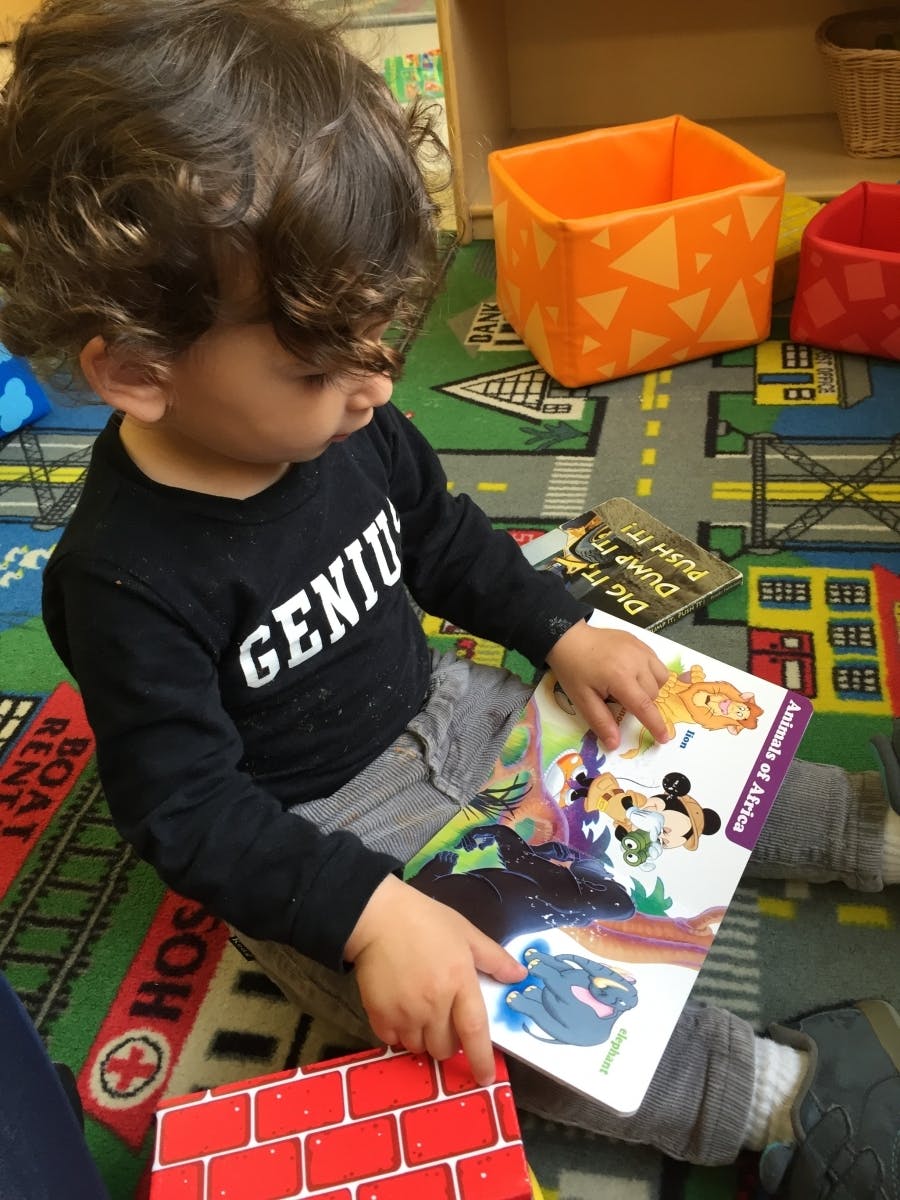 Child sitting on a rug, looking at a book with cartoon animals