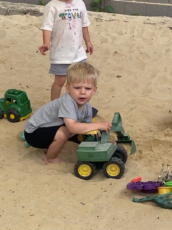 Child playing with a toy excavator in sand