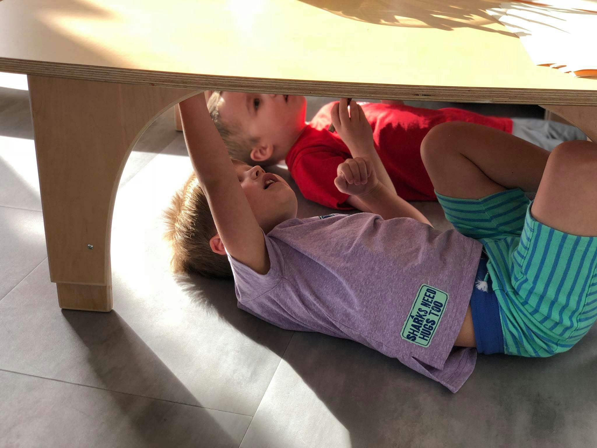 Two children lying under a table