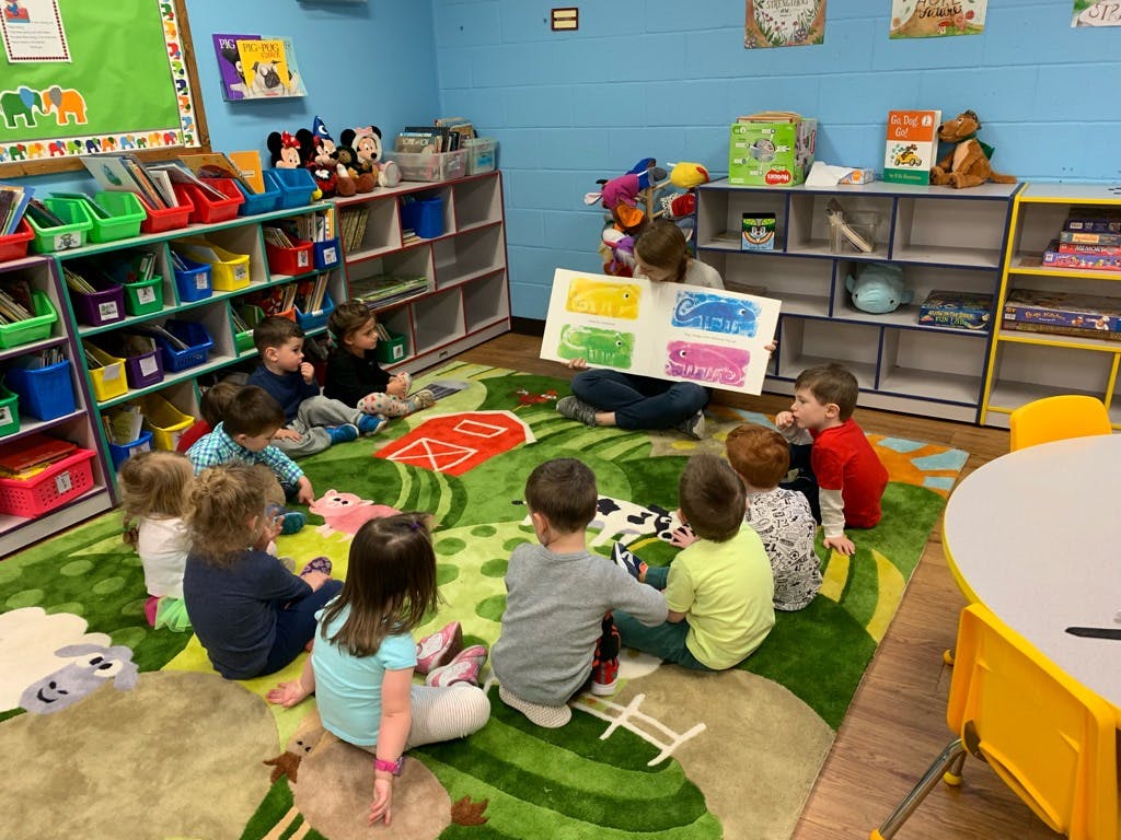 Adult reading a book to a group of children in a classroom