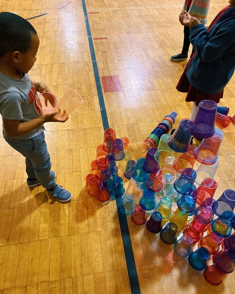Child holding a plastic cup next to a stack of colorful plastic cups