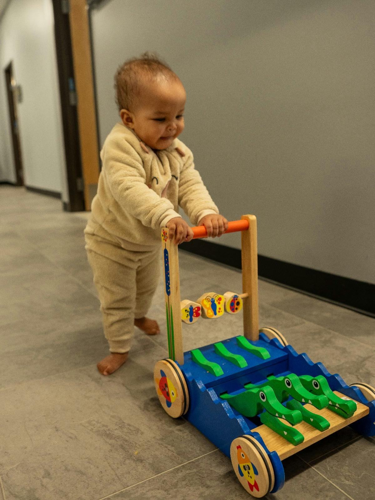 Child standing and pushing a wooden walker toy