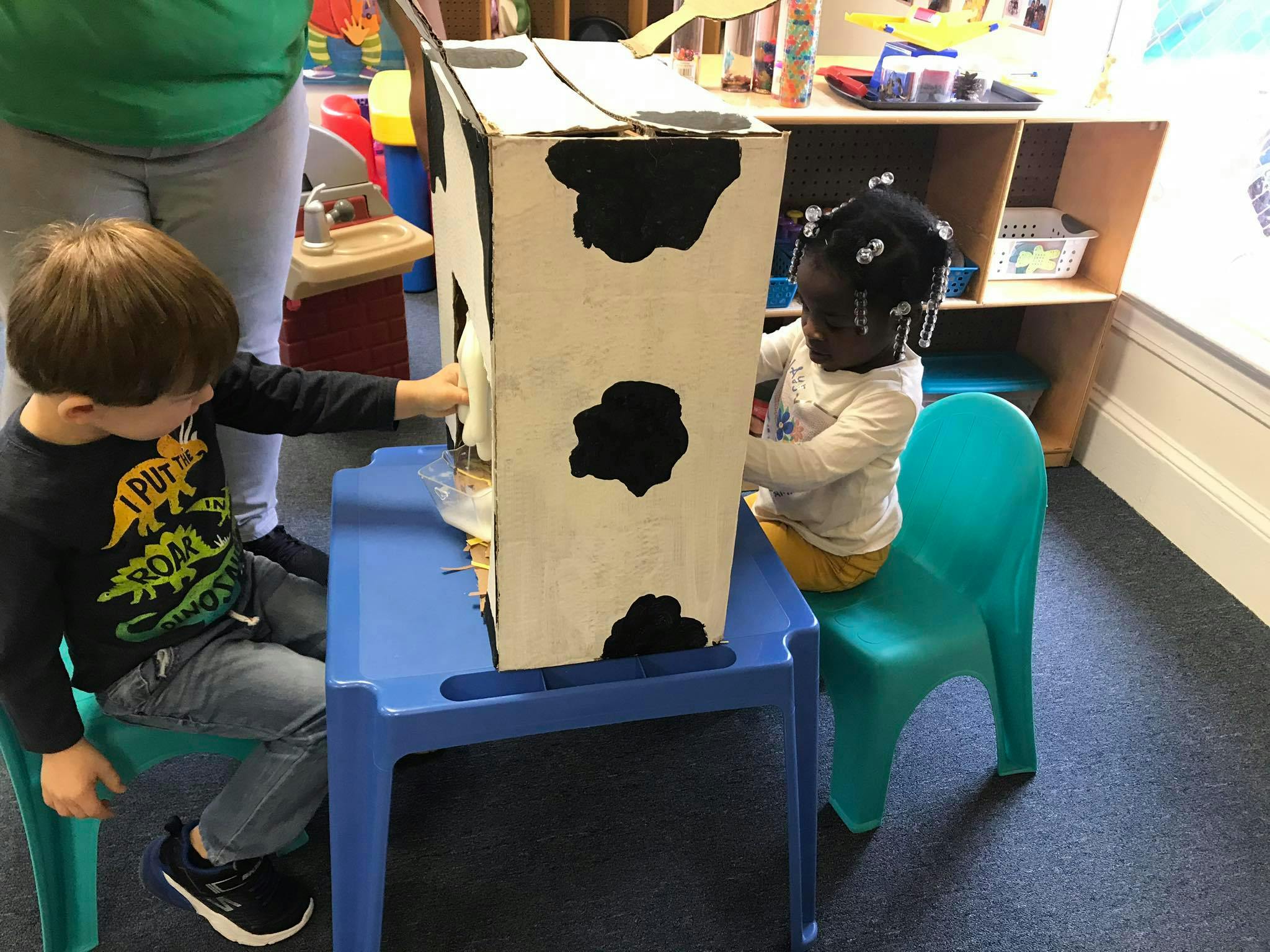 Two children playing with a cow-themed cardboard box