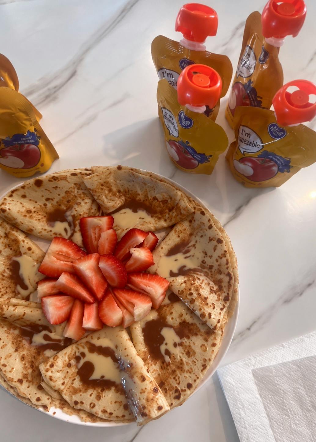 Plate of folded crepes topped with sliced strawberries and sauce pouches