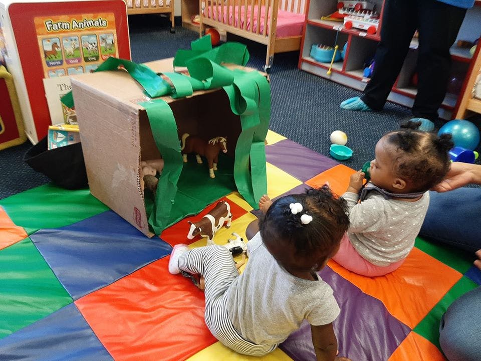 Two children playing with a cardboard box decorated as a barn with toy animals