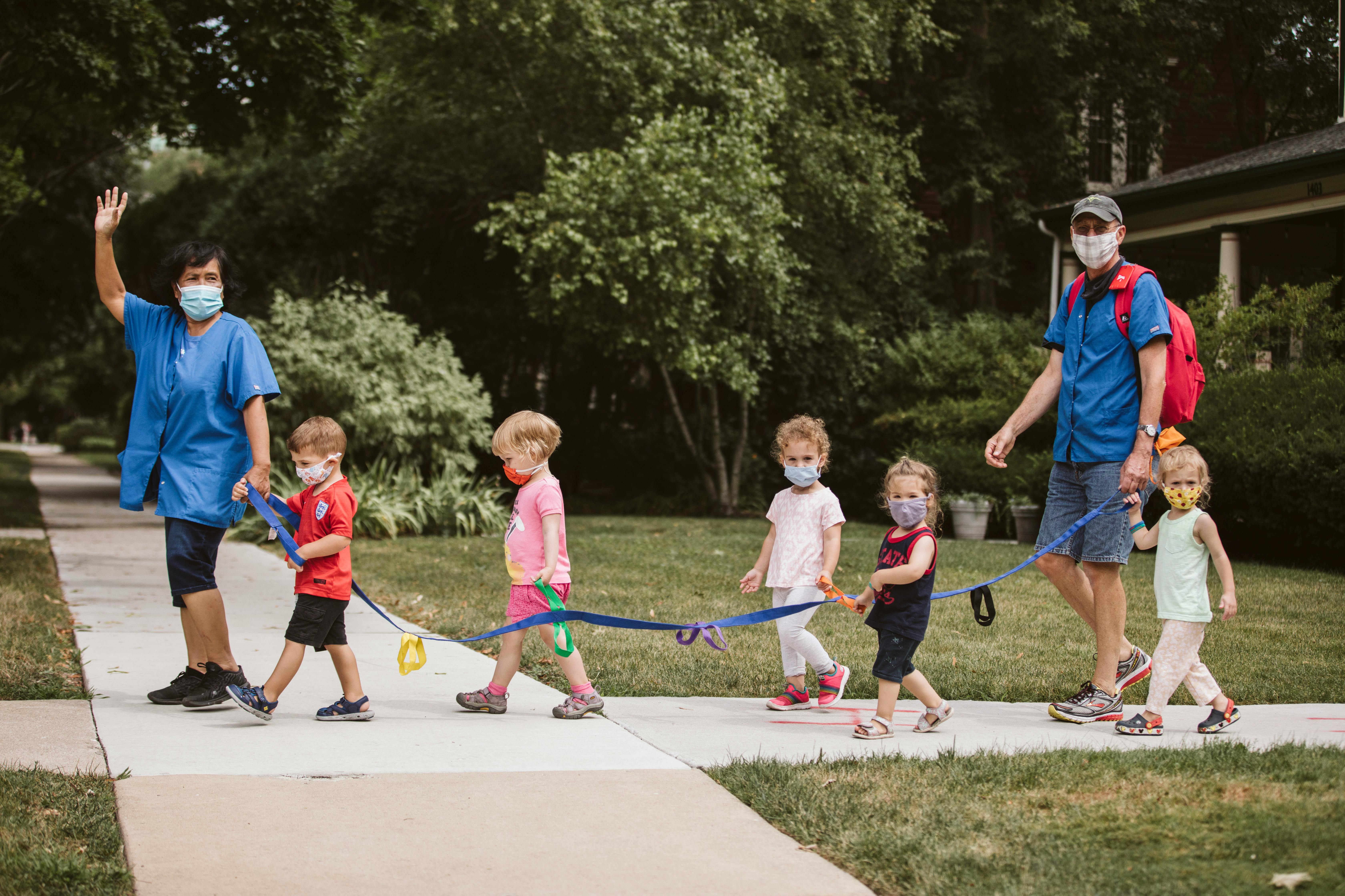 Two adults and five children wearing masks walking on a sidewalk