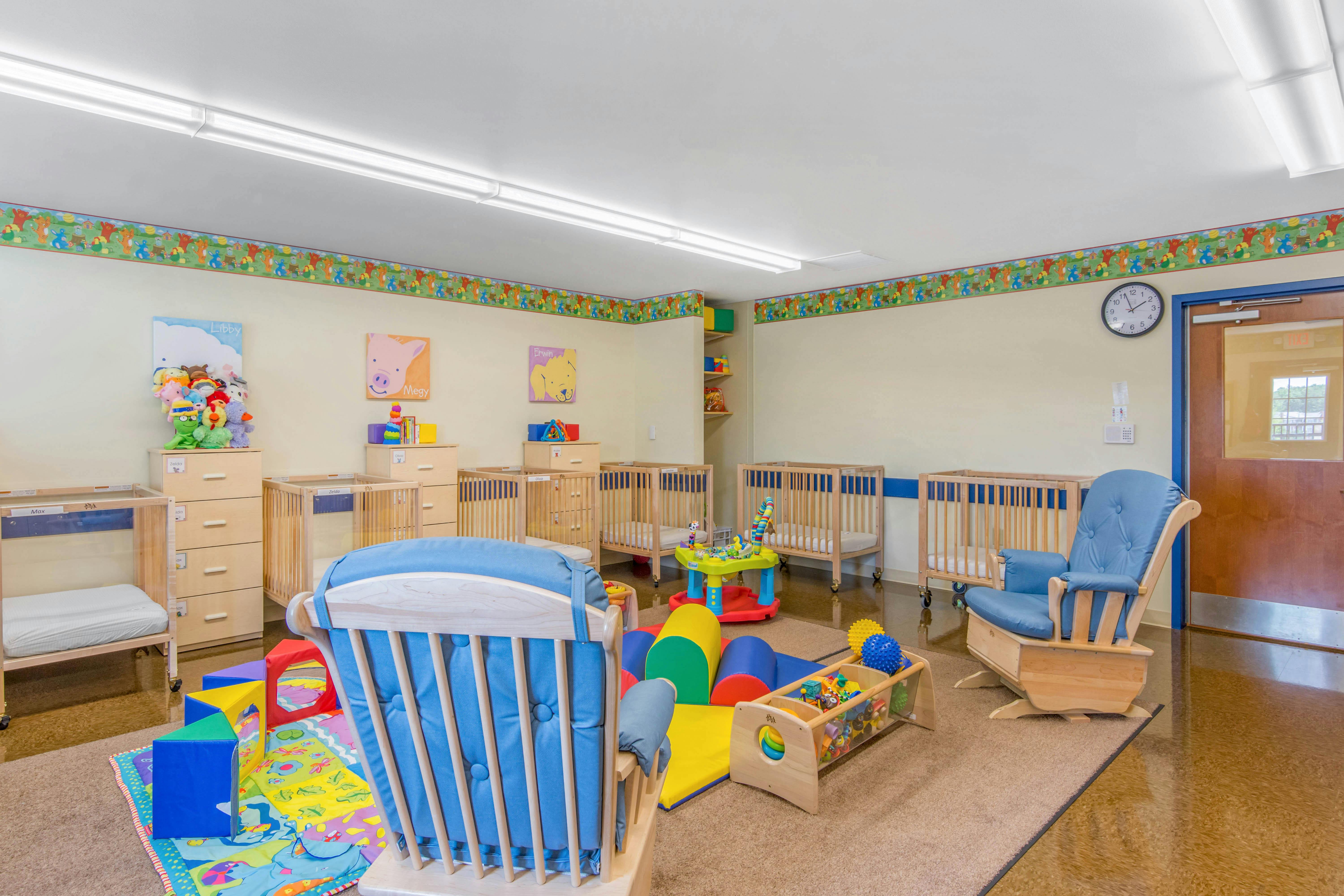 A childcare room with cribs, play mats, and a rocking chair