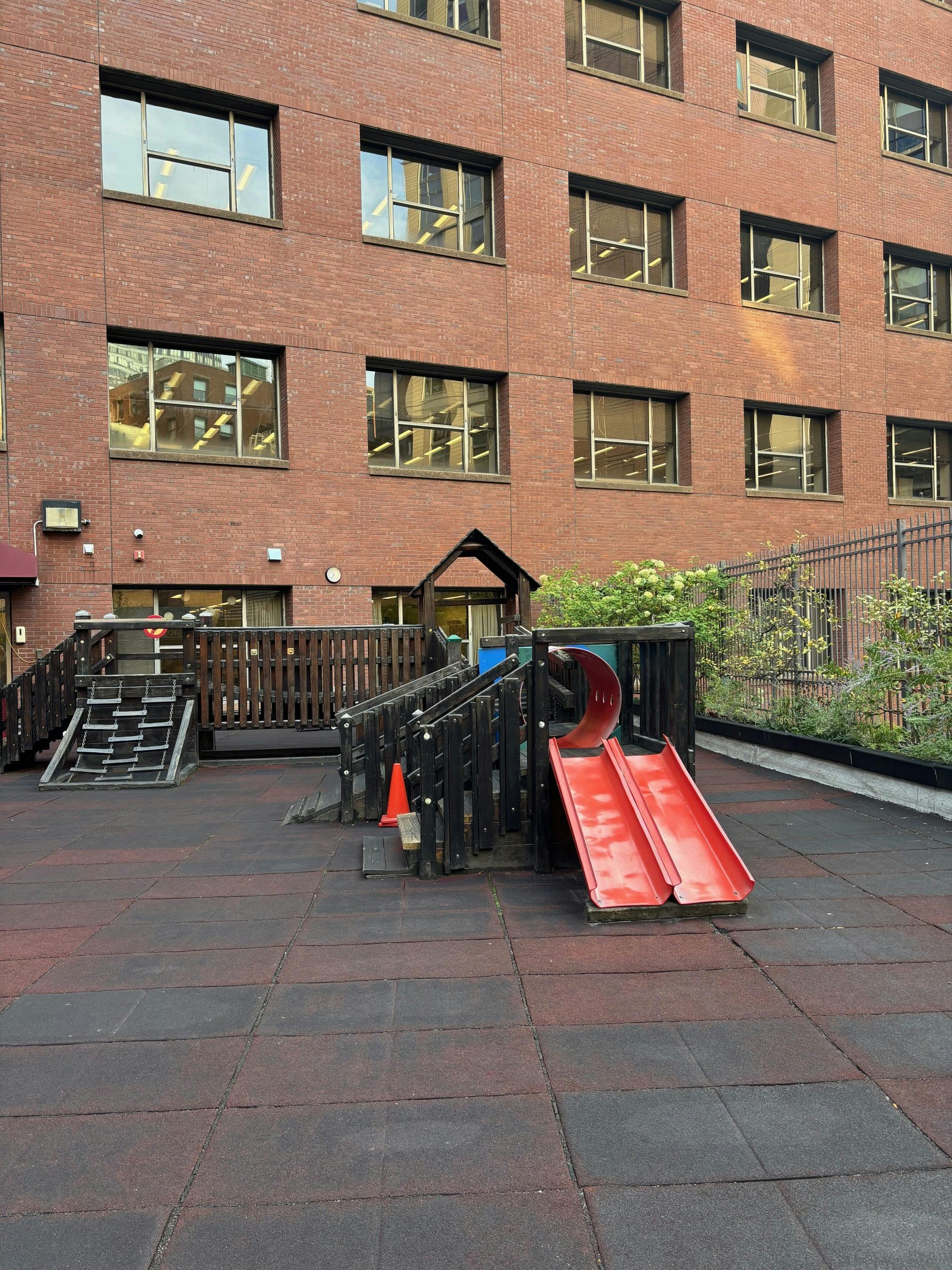 Playground with red slides and climbing structure in front of a brick building