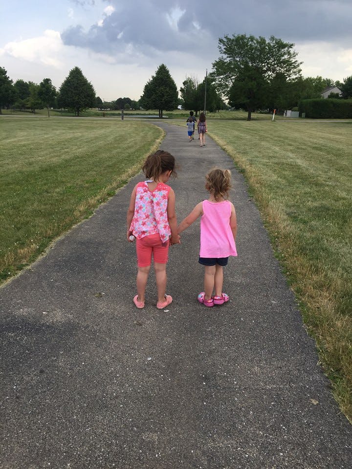 Two children holding hands on a path, with other children walking ahead