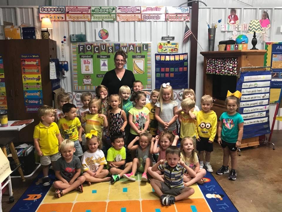 Adult and many children posing in a classroom