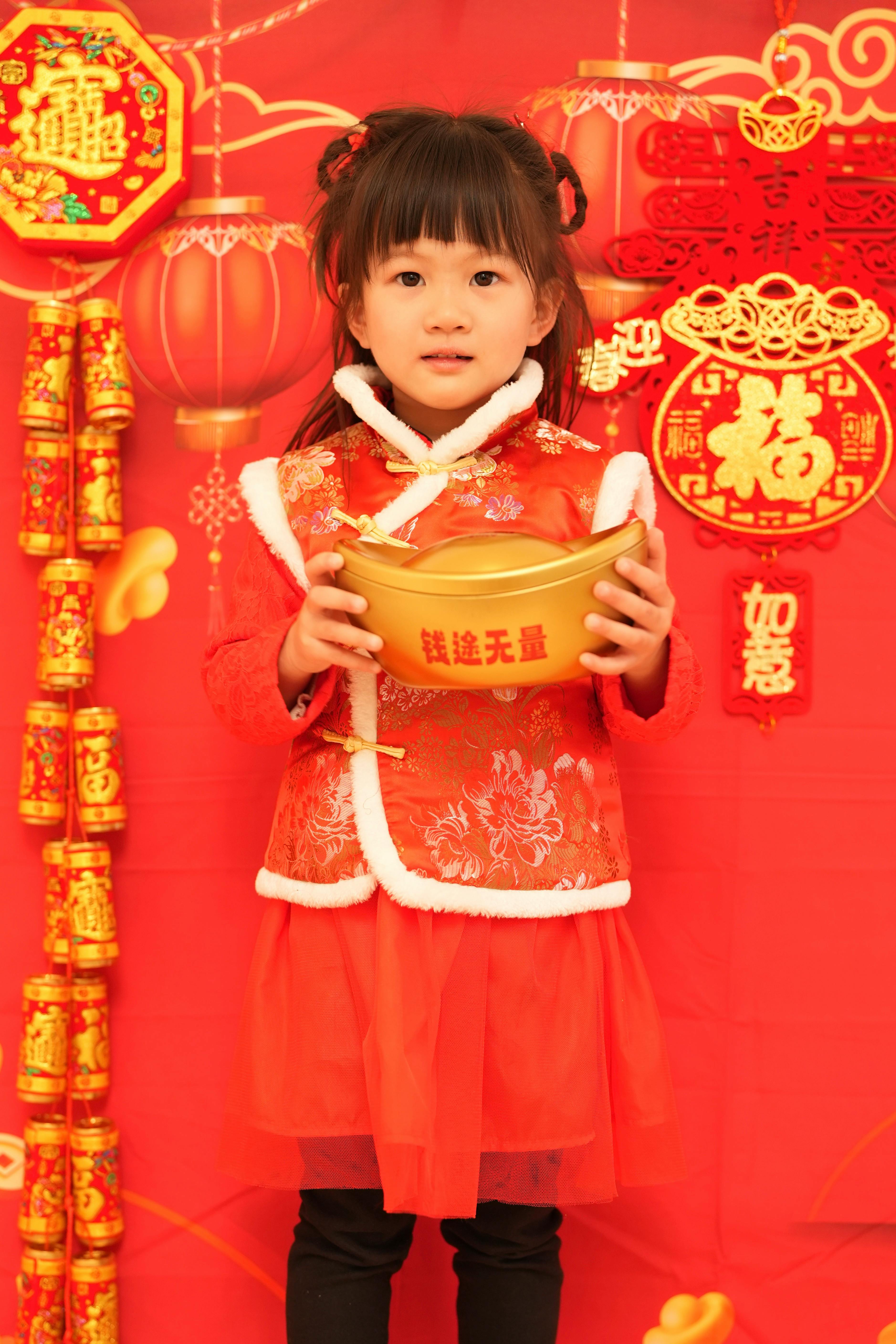 Child in traditional red clothing holding a golden ingot