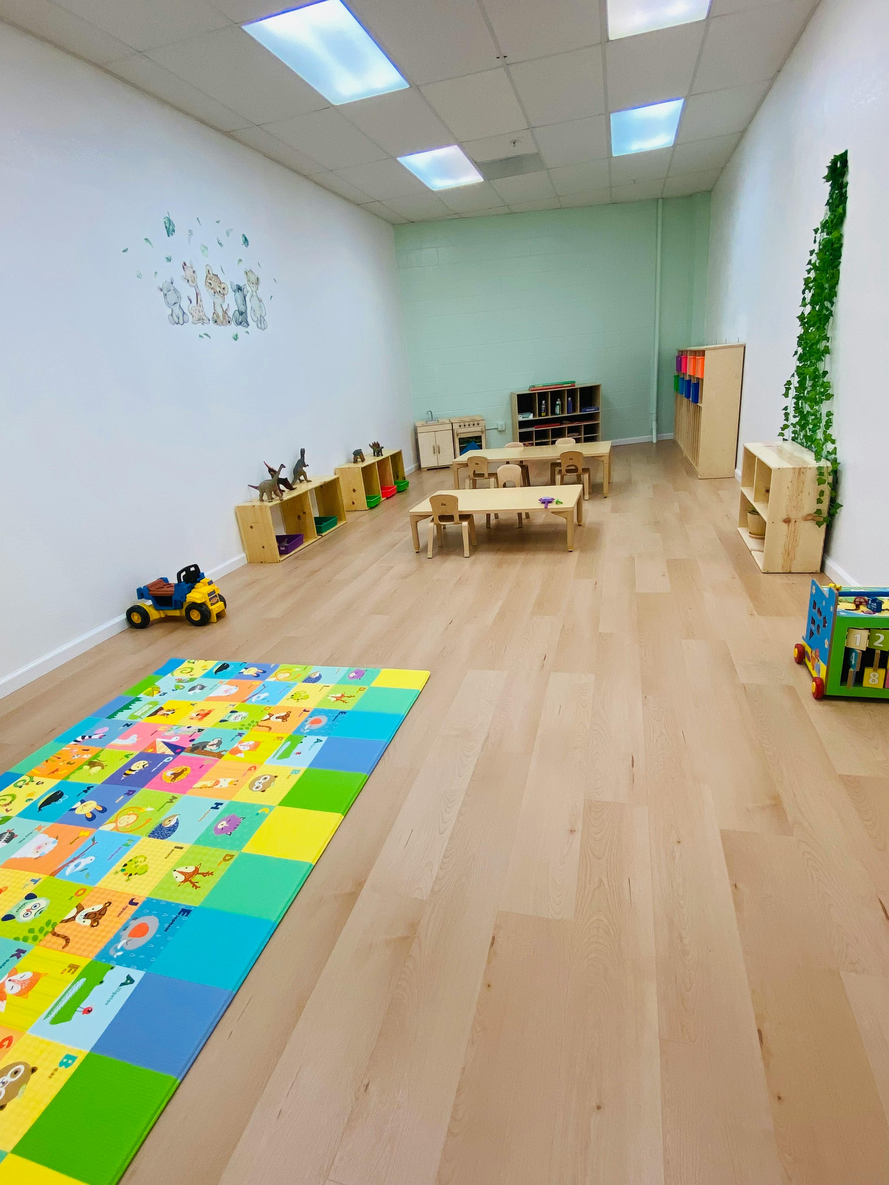 Empty classroom with small tables and chairs, colorful playmat on floor