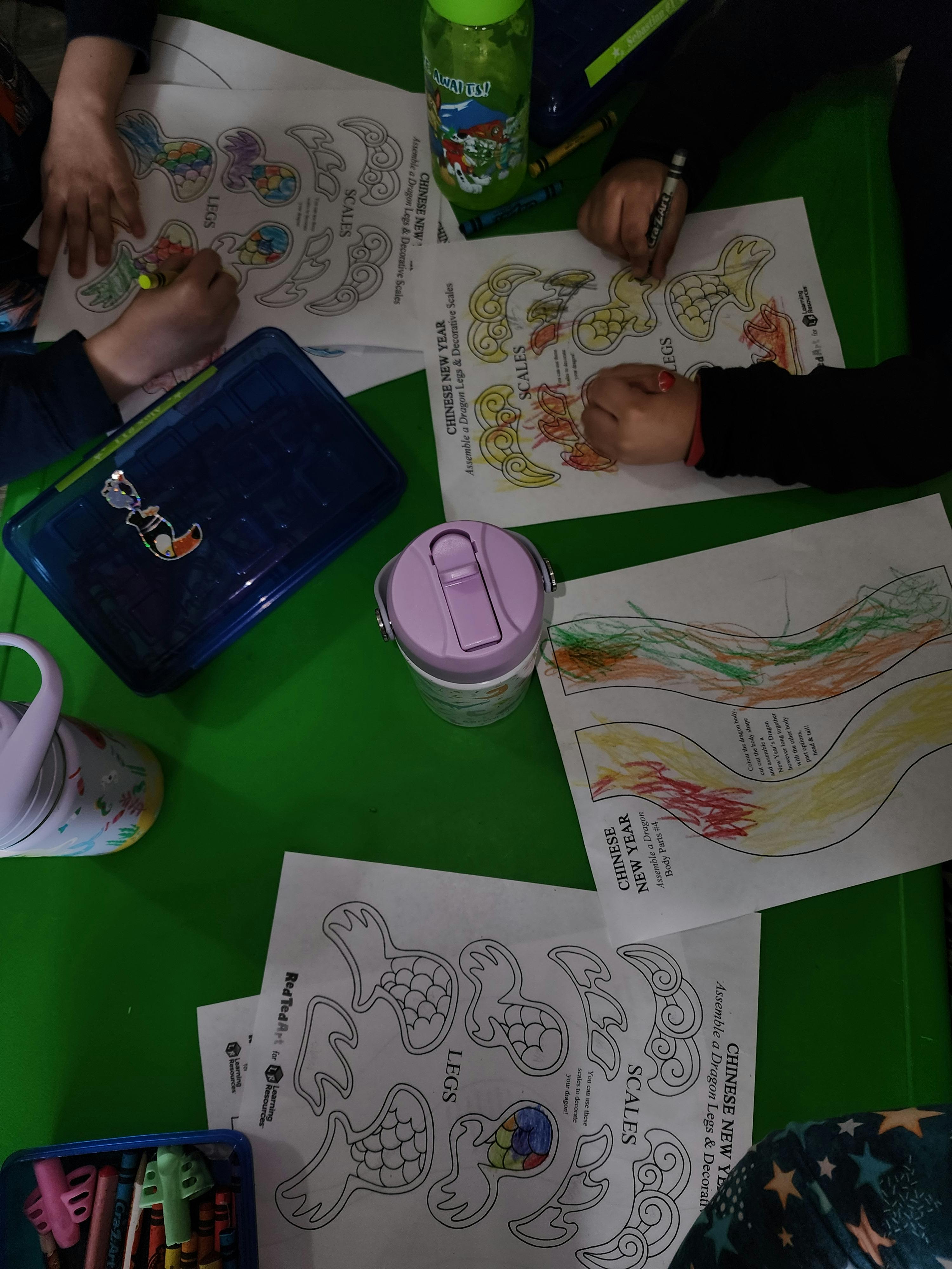 Children coloring Chinese New Year themed pages at a green table