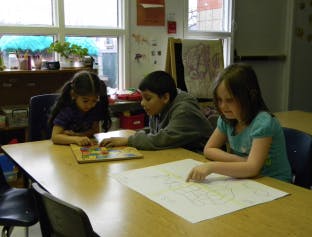 Three children at a table, one playing a board game, one looking at a map