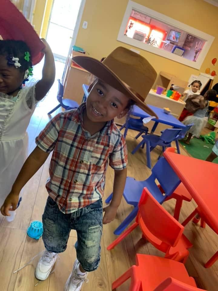 Child in a cowboy hat and plaid shirt smiling in a classroom
