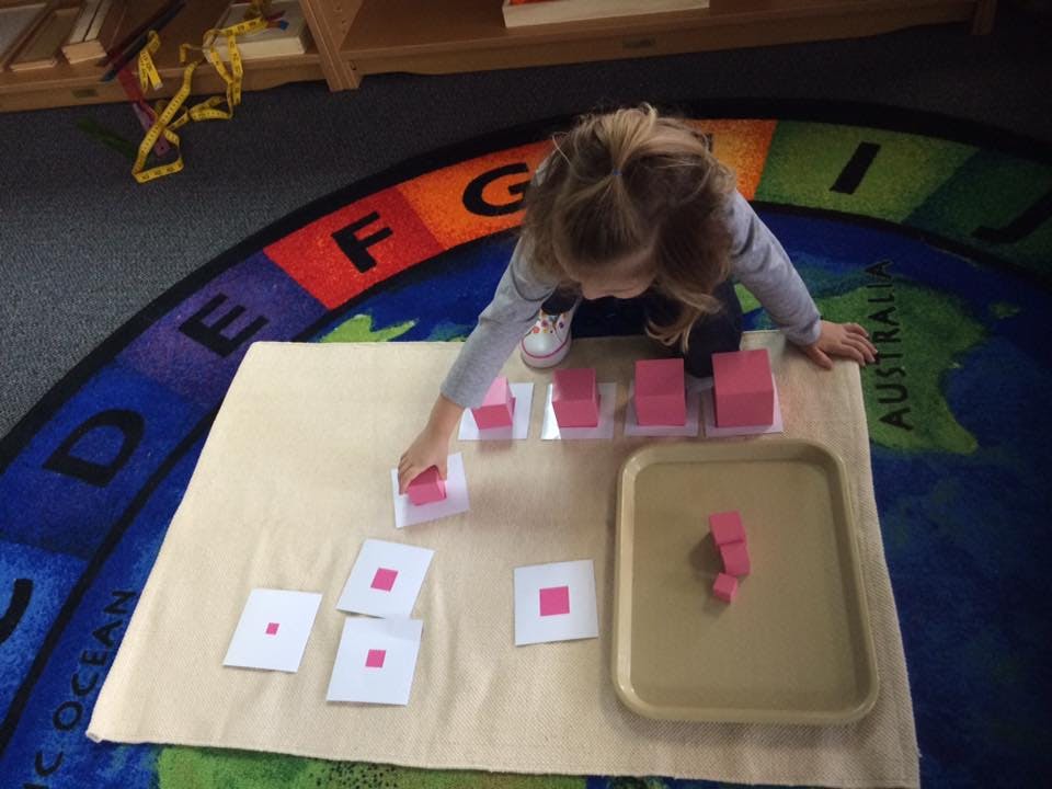 Child playing with pink blocks and cards on a rug