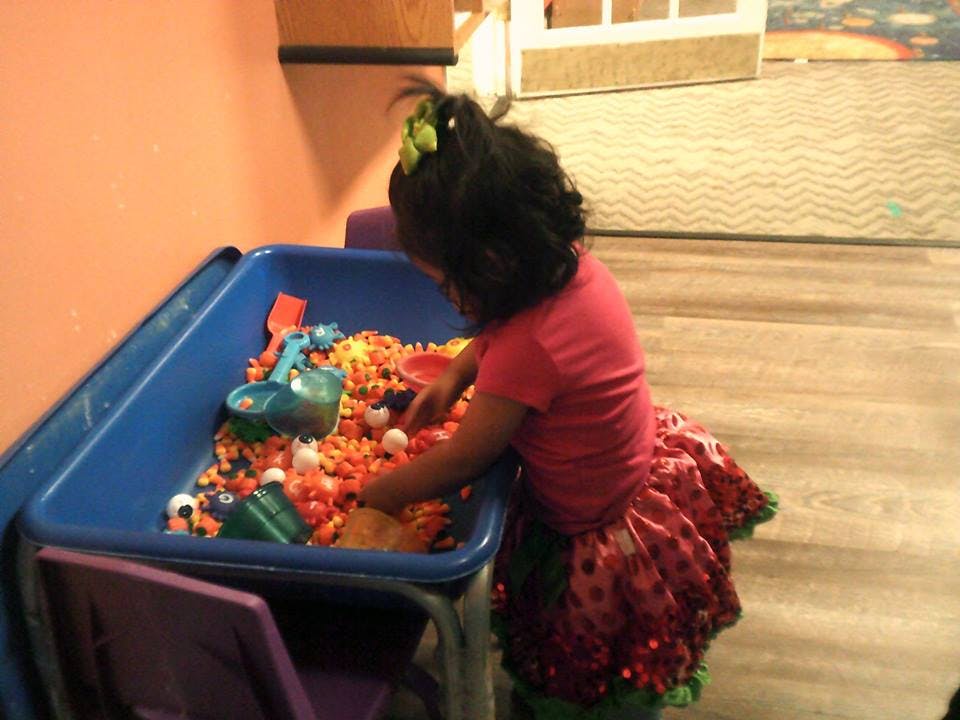 Child playing in a sensory bin filled with small orange objects