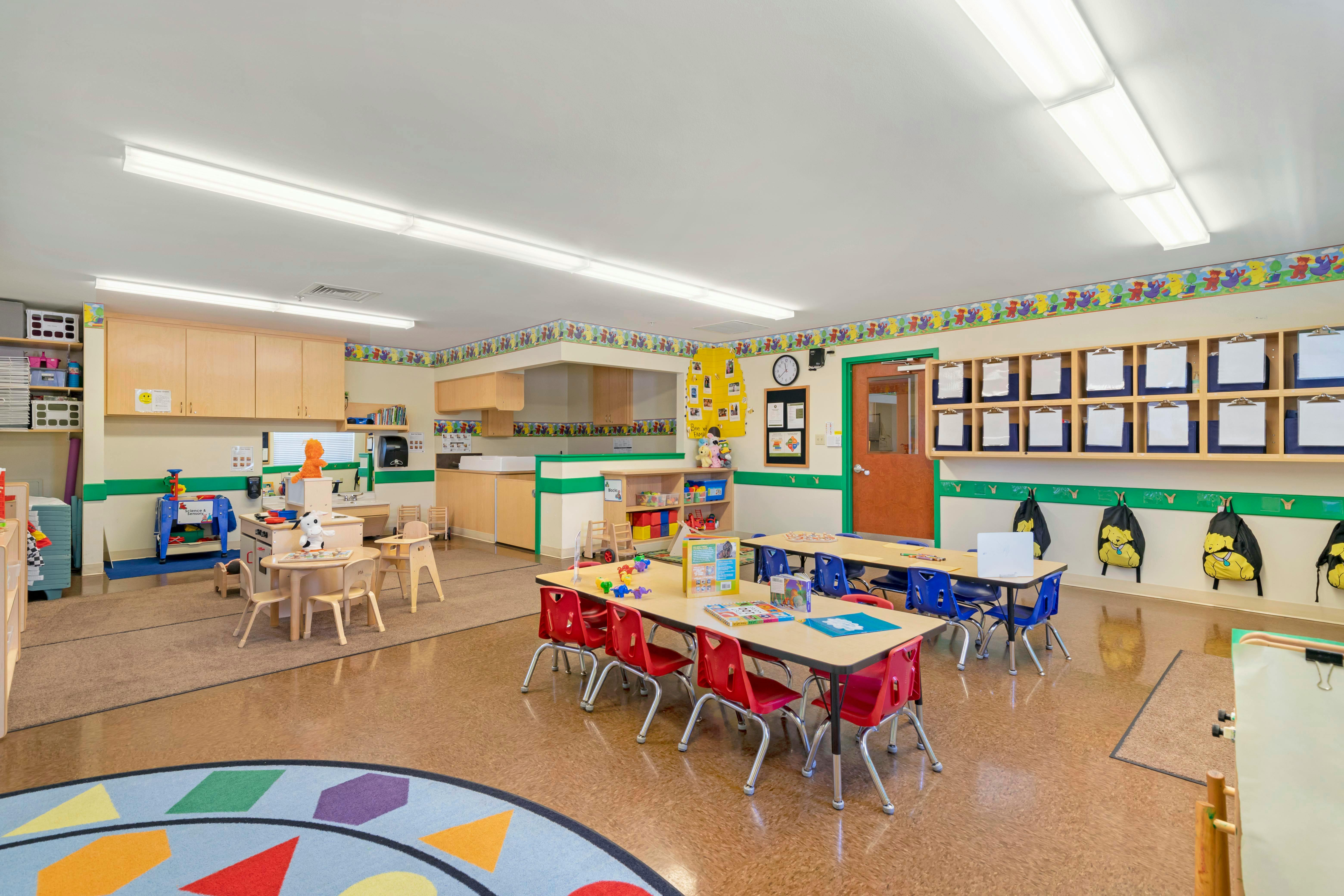 Empty classroom with small tables and chairs, play kitchen, and storage units