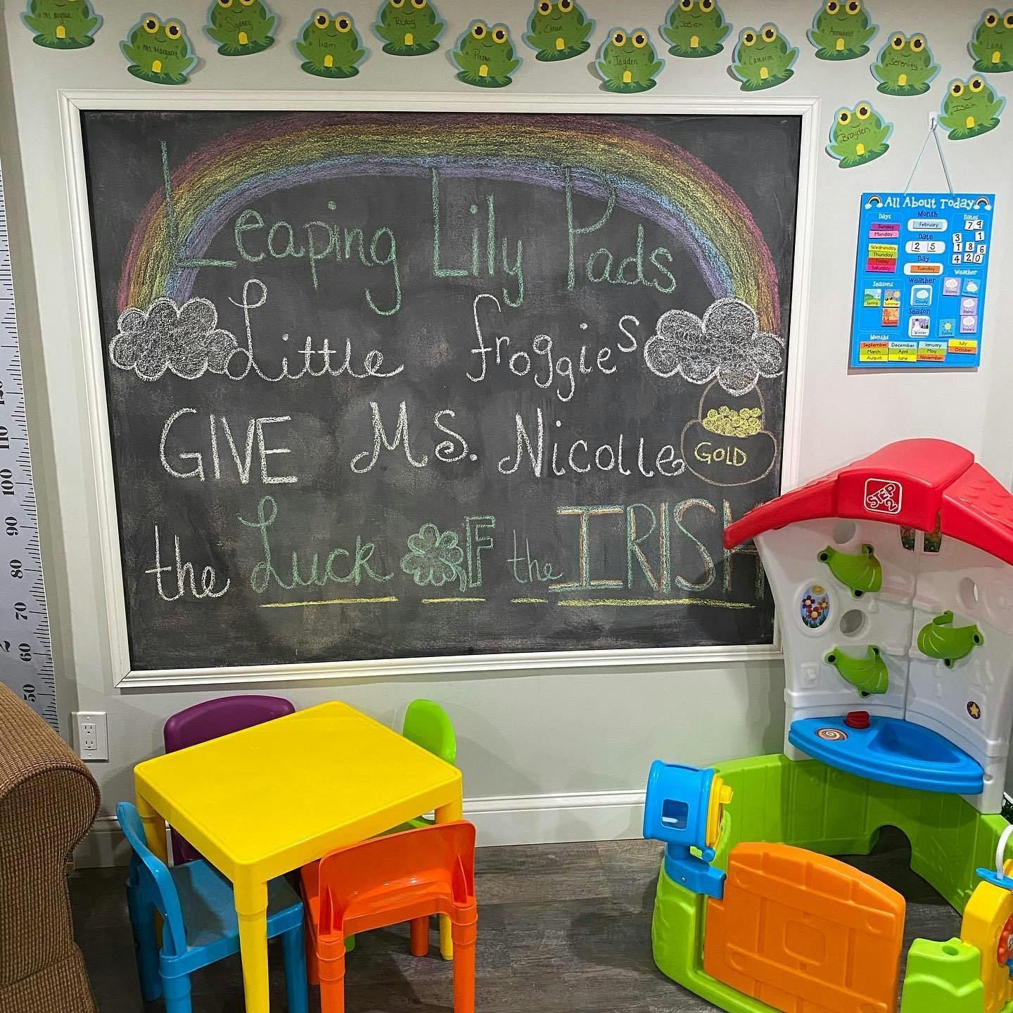 Chalkboard with rainbow and text, small table and chairs, and play structure