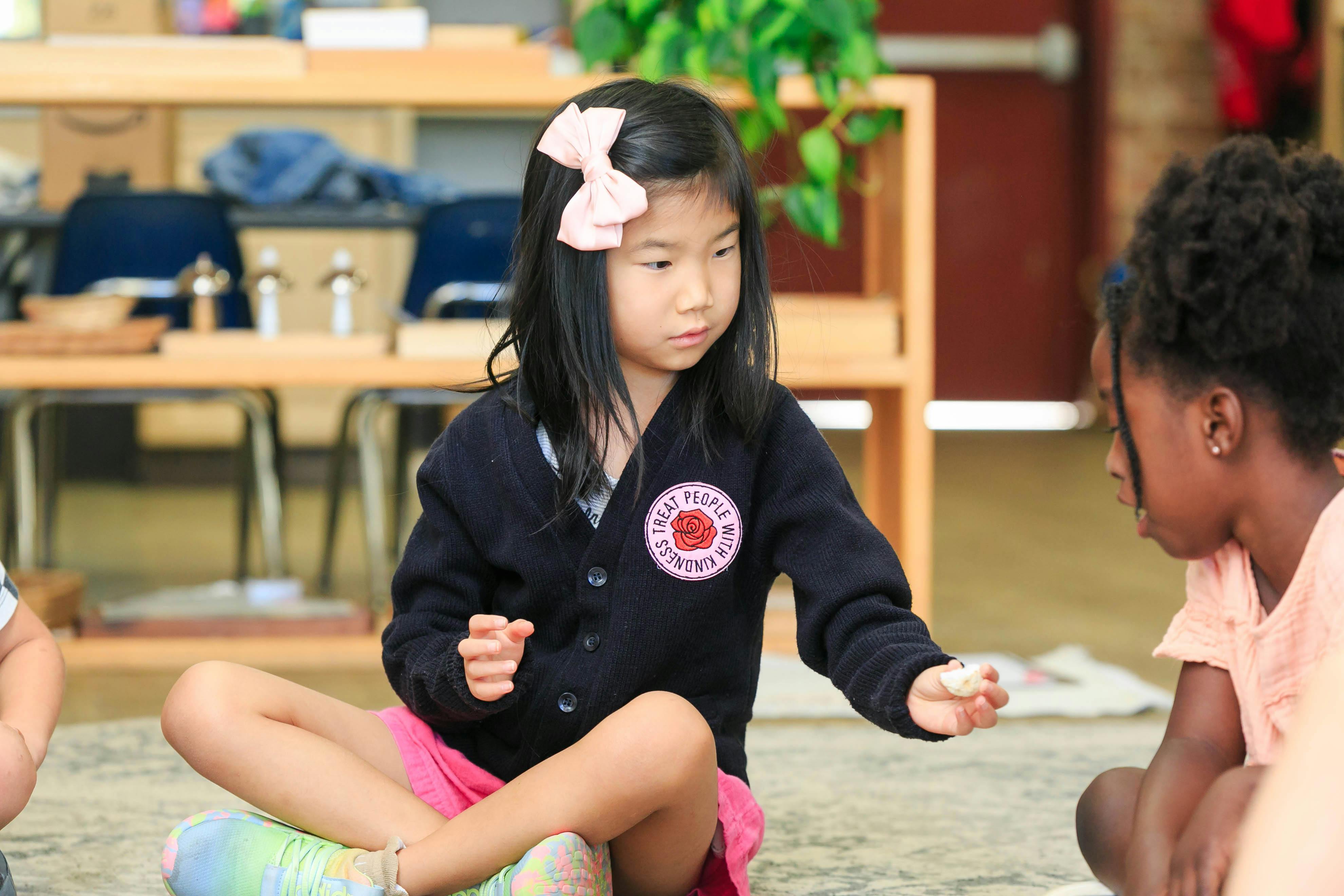 Child sitting on floor, holding out an object to another child