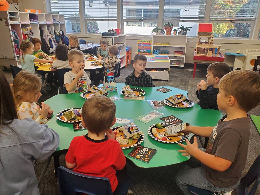 Children eating at a green table in a classroom