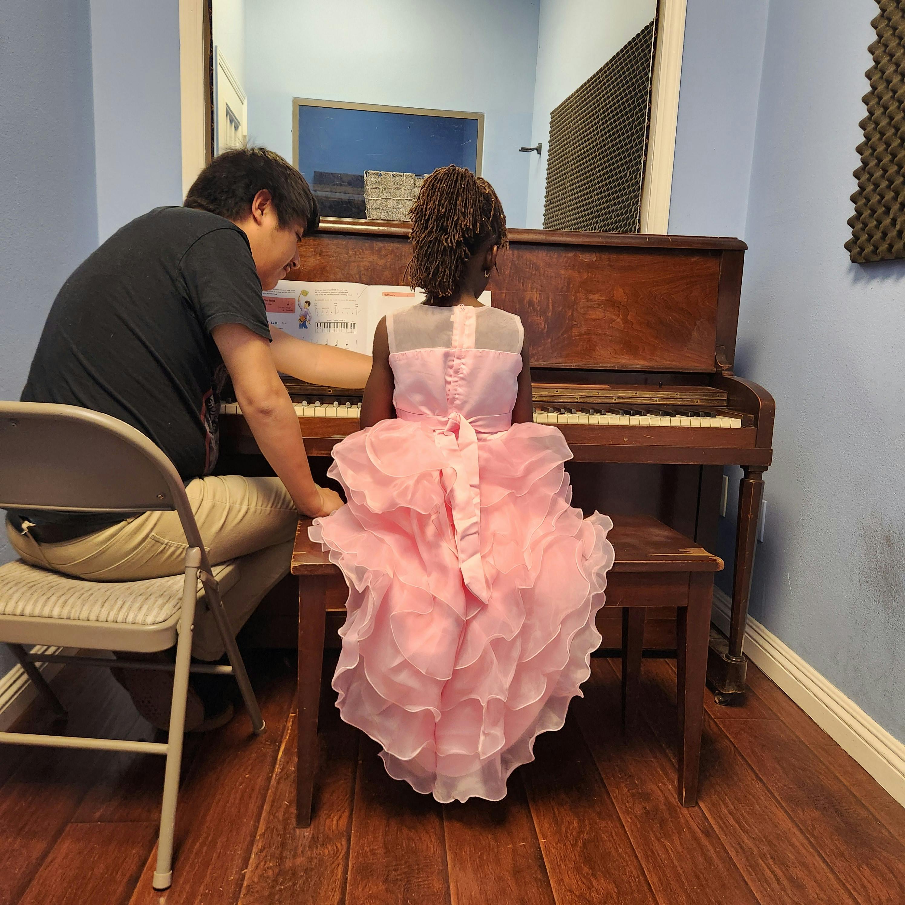 Child in pink dress learning piano from an adult