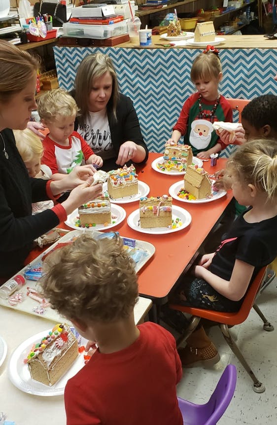 Adults and children decorating gingerbread houses at a table