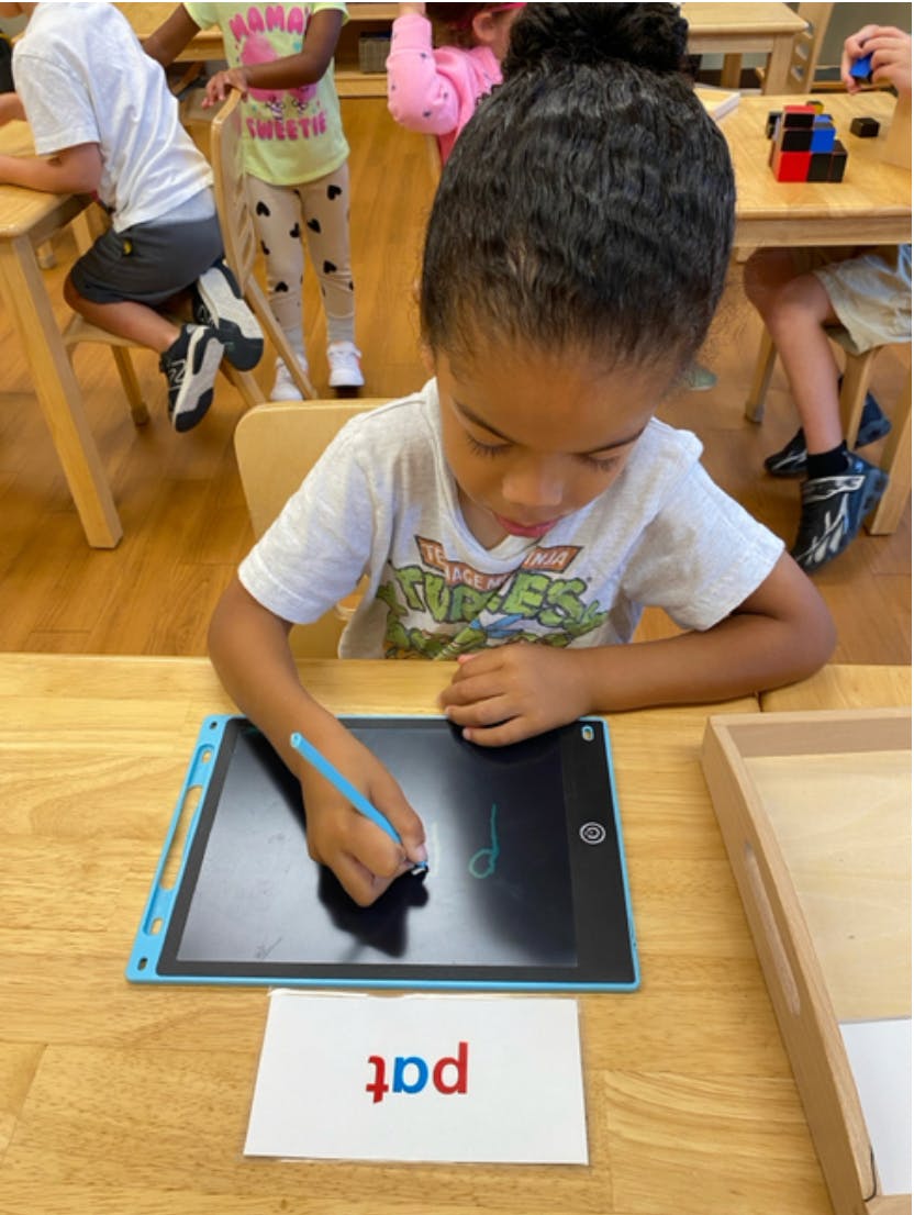 Child writing on a digital tablet with a stylus, word "pat" on card