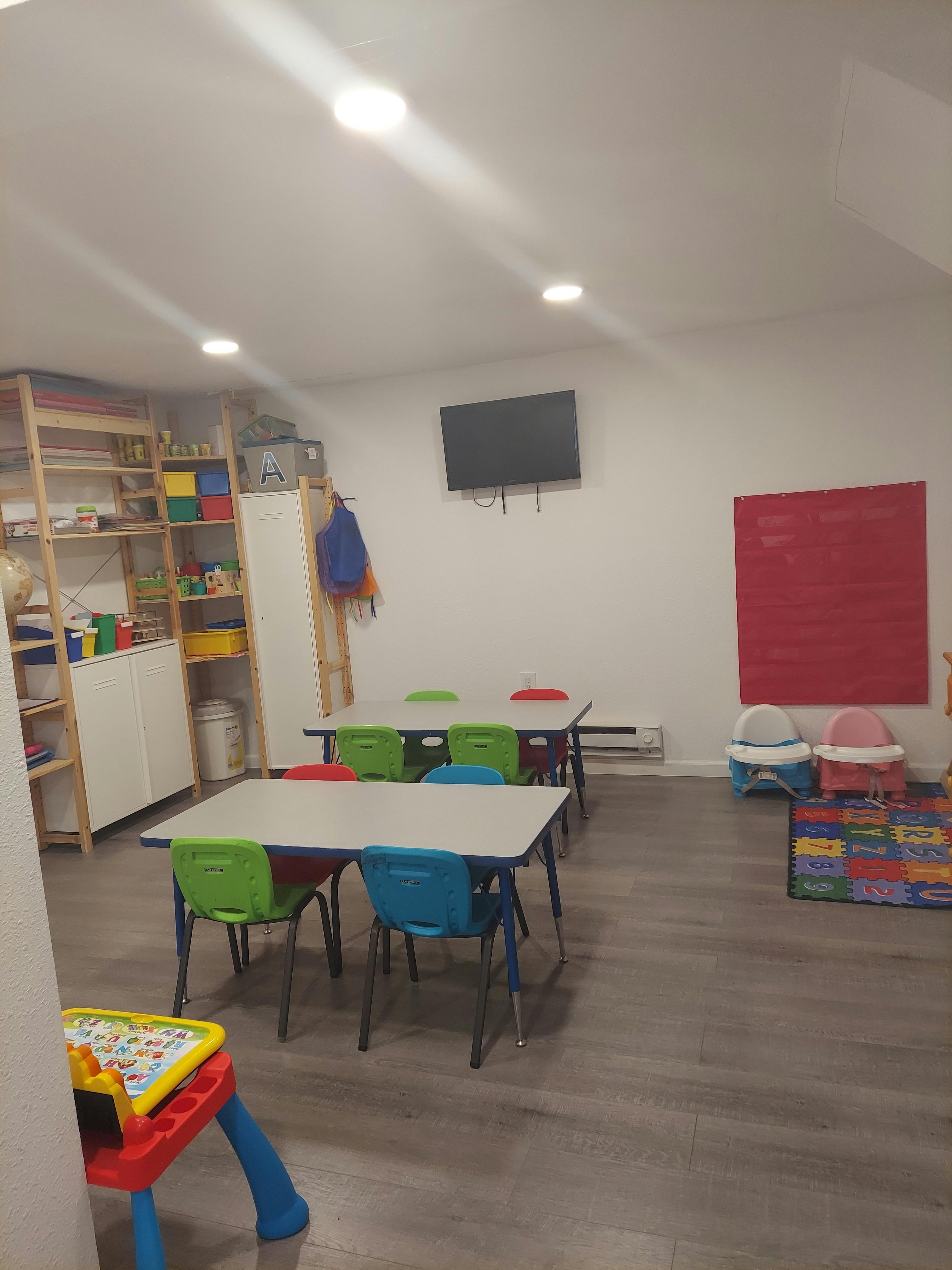 Classroom with small tables and chairs, shelves, and a wall-mounted TV