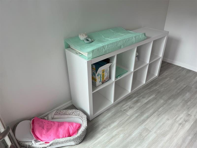 Changing pad on a white storage unit next to a baby bassinet