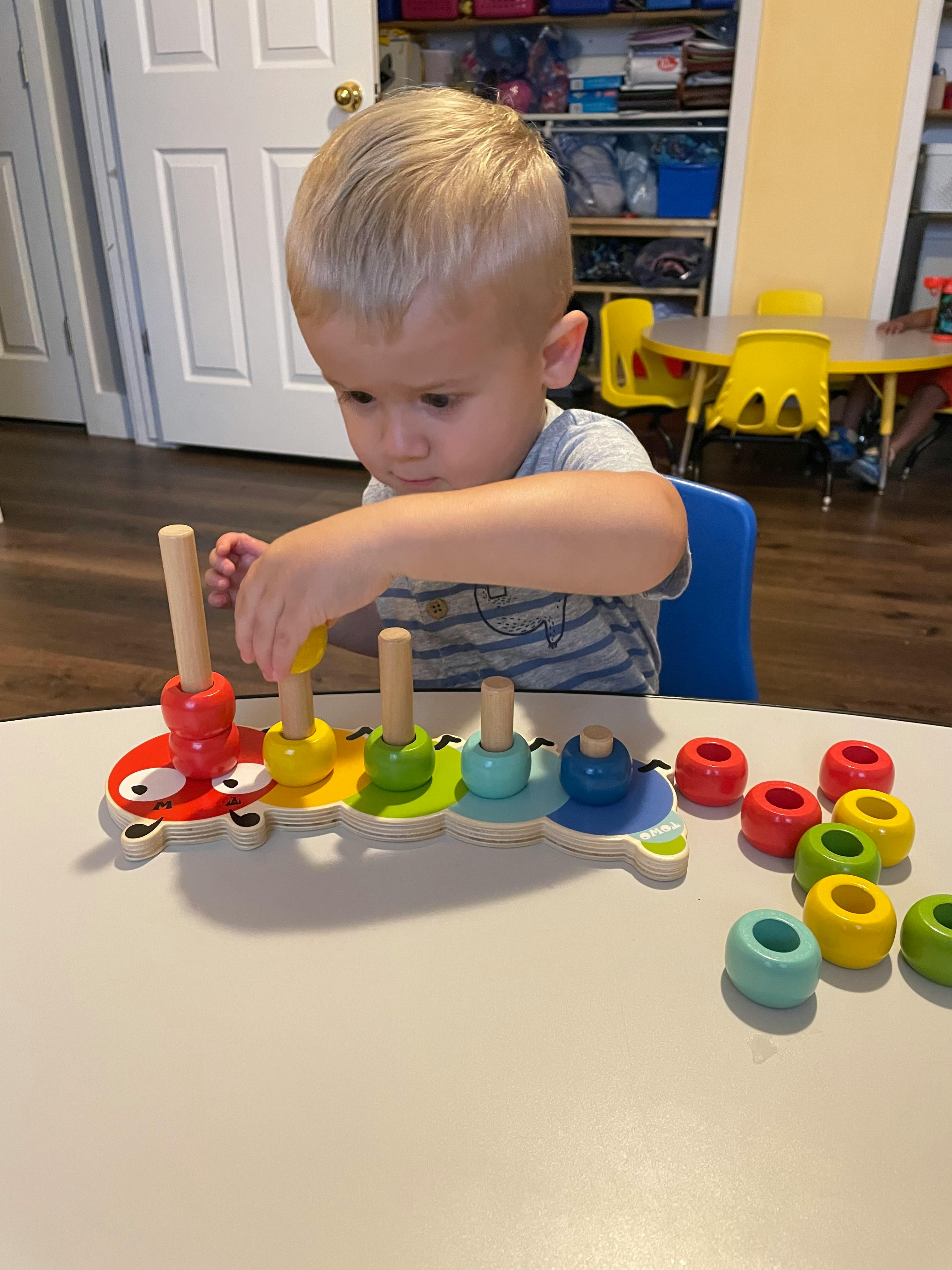 Child playing with a colorful stacking toy on a table