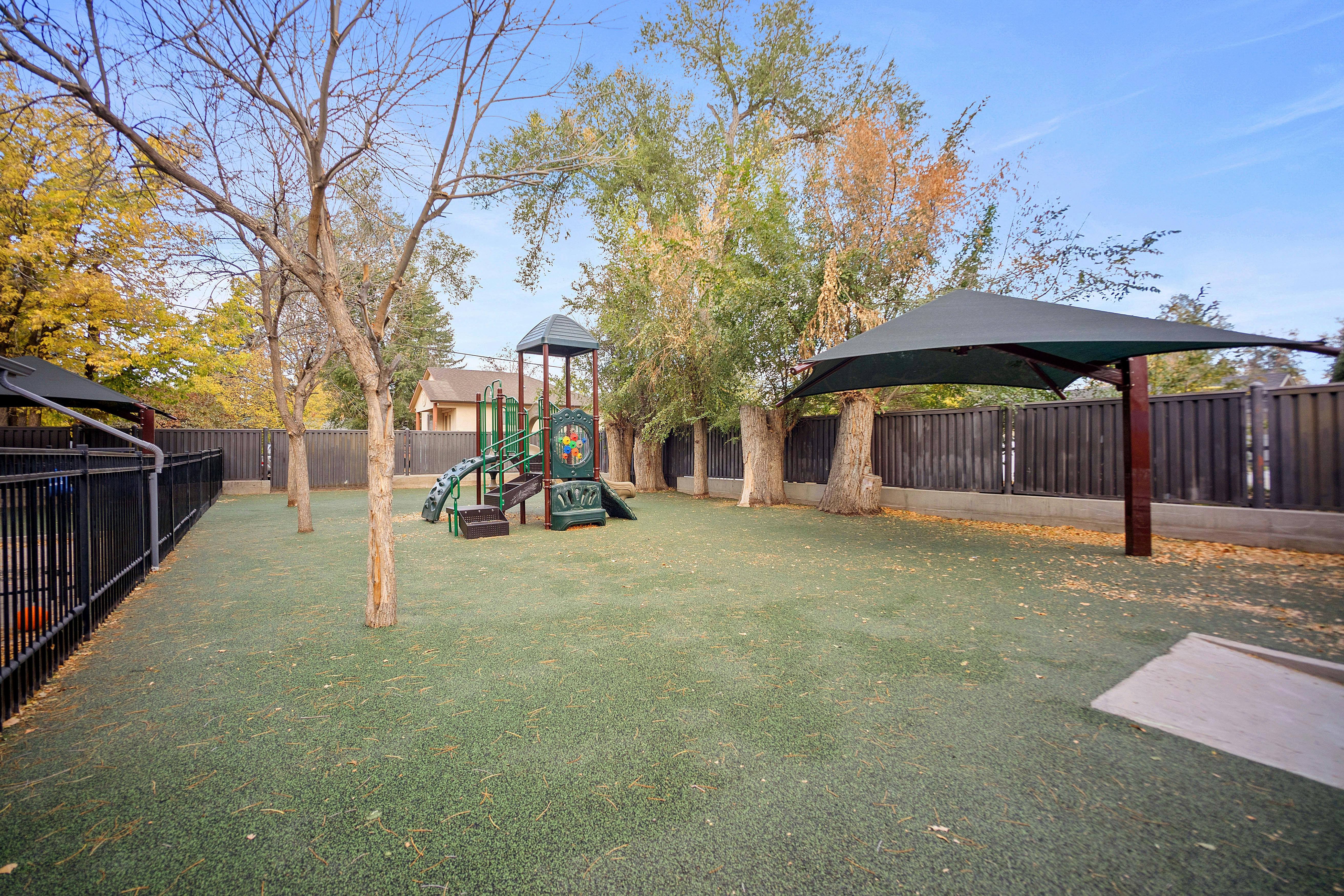 An outdoor playground with a climbing structure, slides, and shade structures