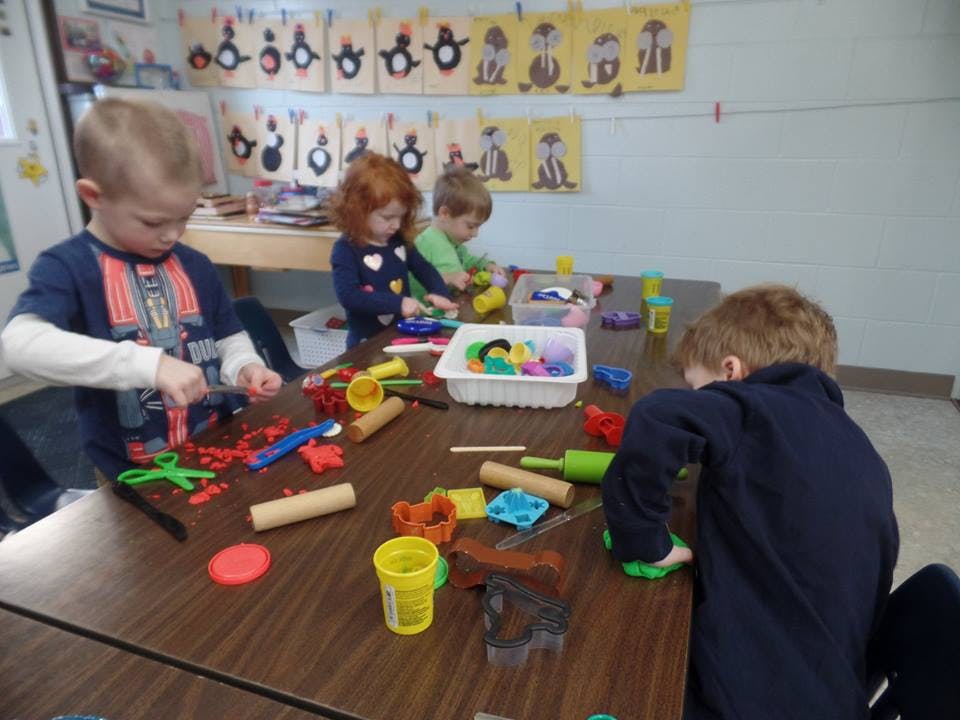 Children playing with modeling clay at a table in a classroom