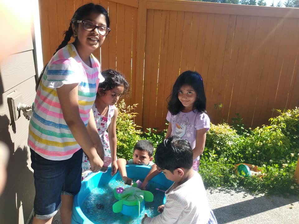 Four children and one teen playing with a water table outdoors