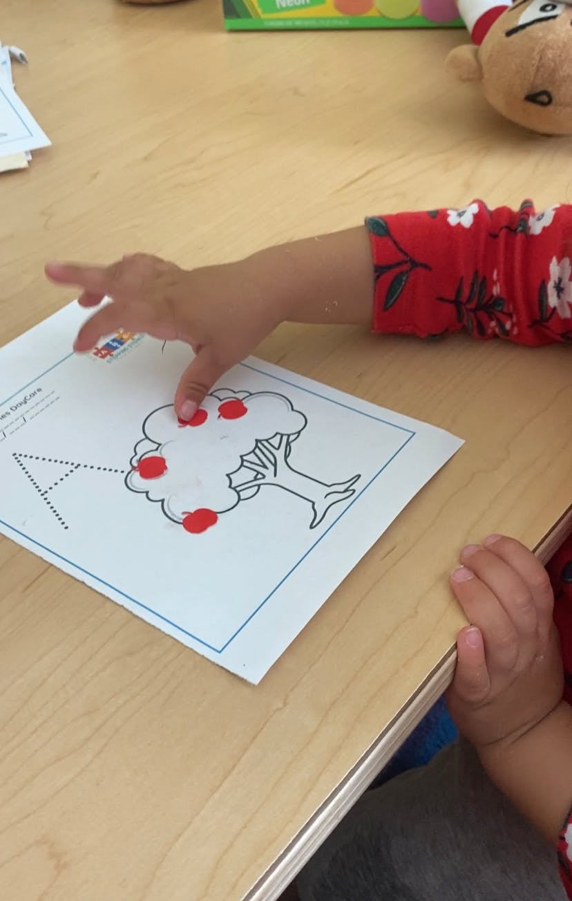 Child placing stickers on a worksheet with a drawing of a tree and letter A