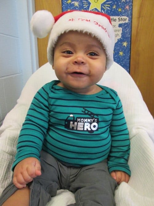 Child wearing a Santa hat and a shirt that says "Mommy's Hero"