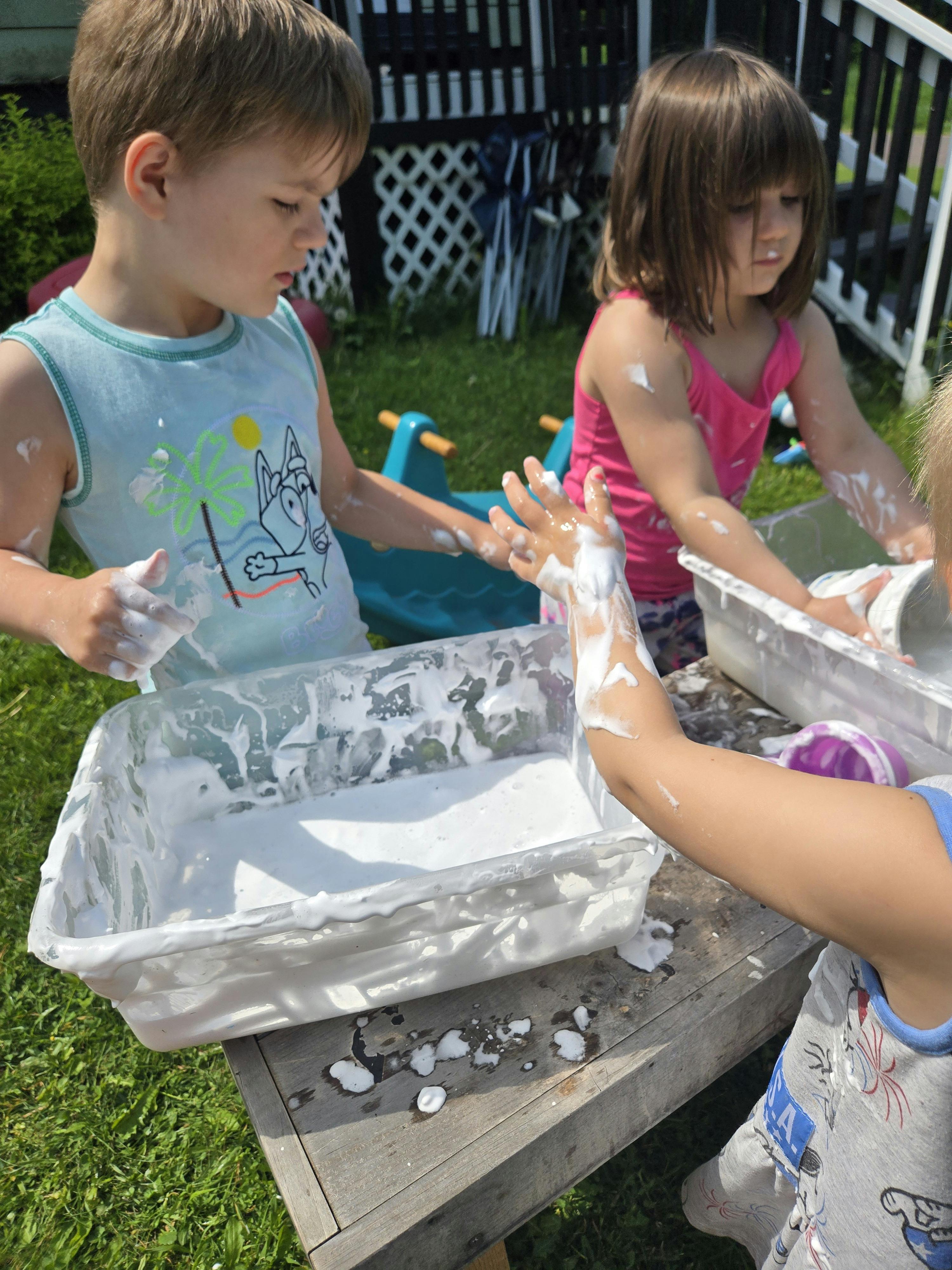 Children playing with foam in plastic bins outdoors