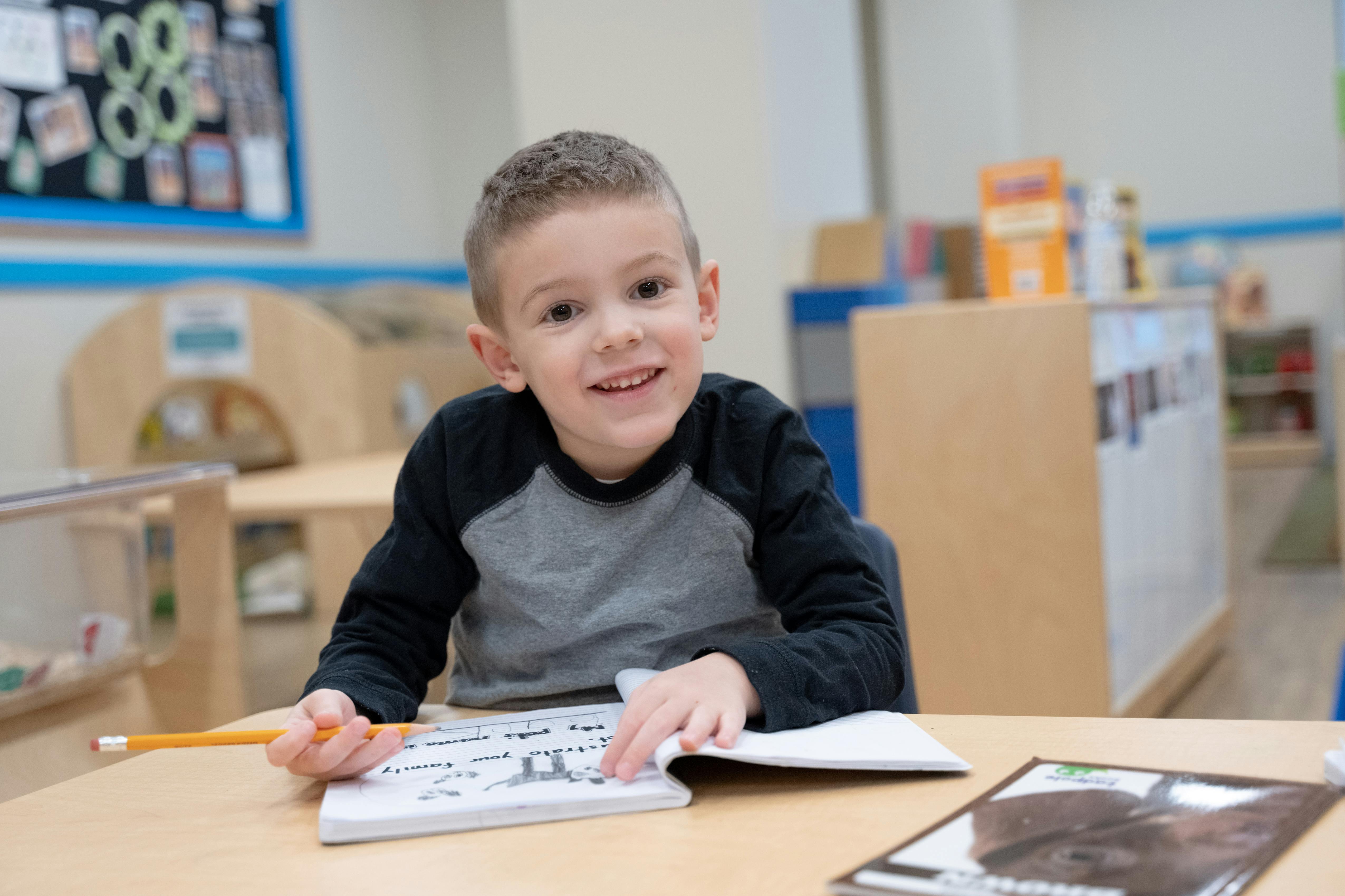 Child at a desk with a pencil and open notebook in a classroom