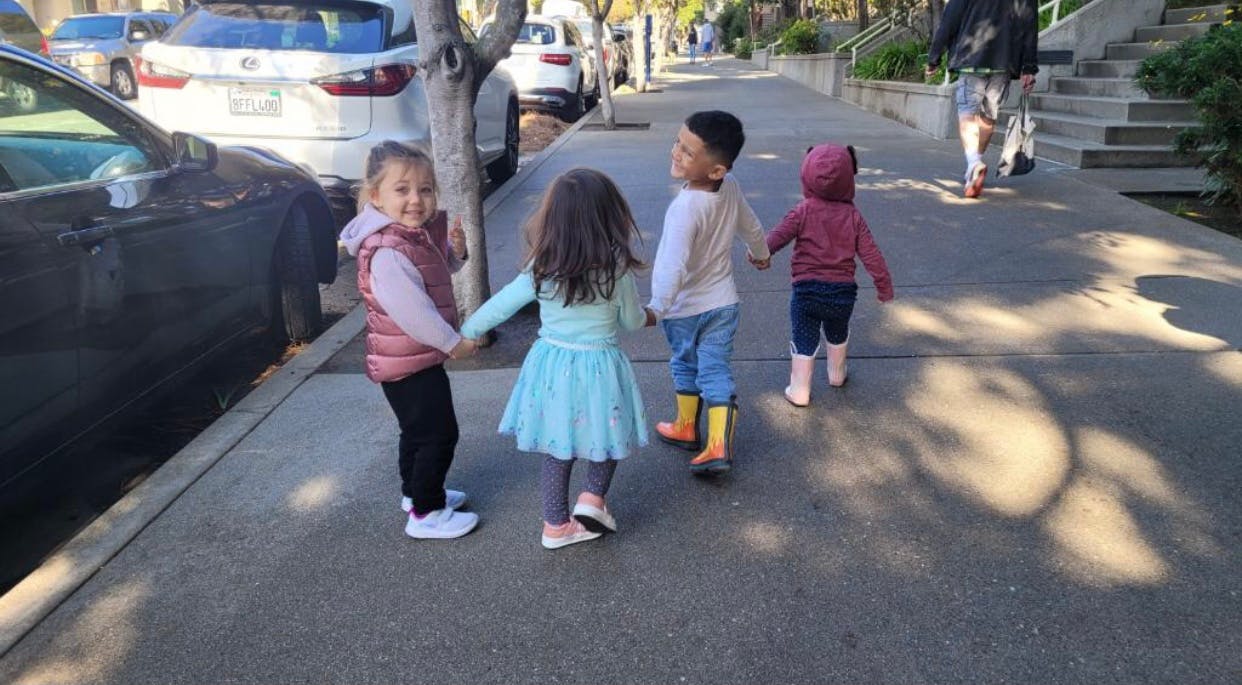 Four children walking on a sidewalk, holding hands
