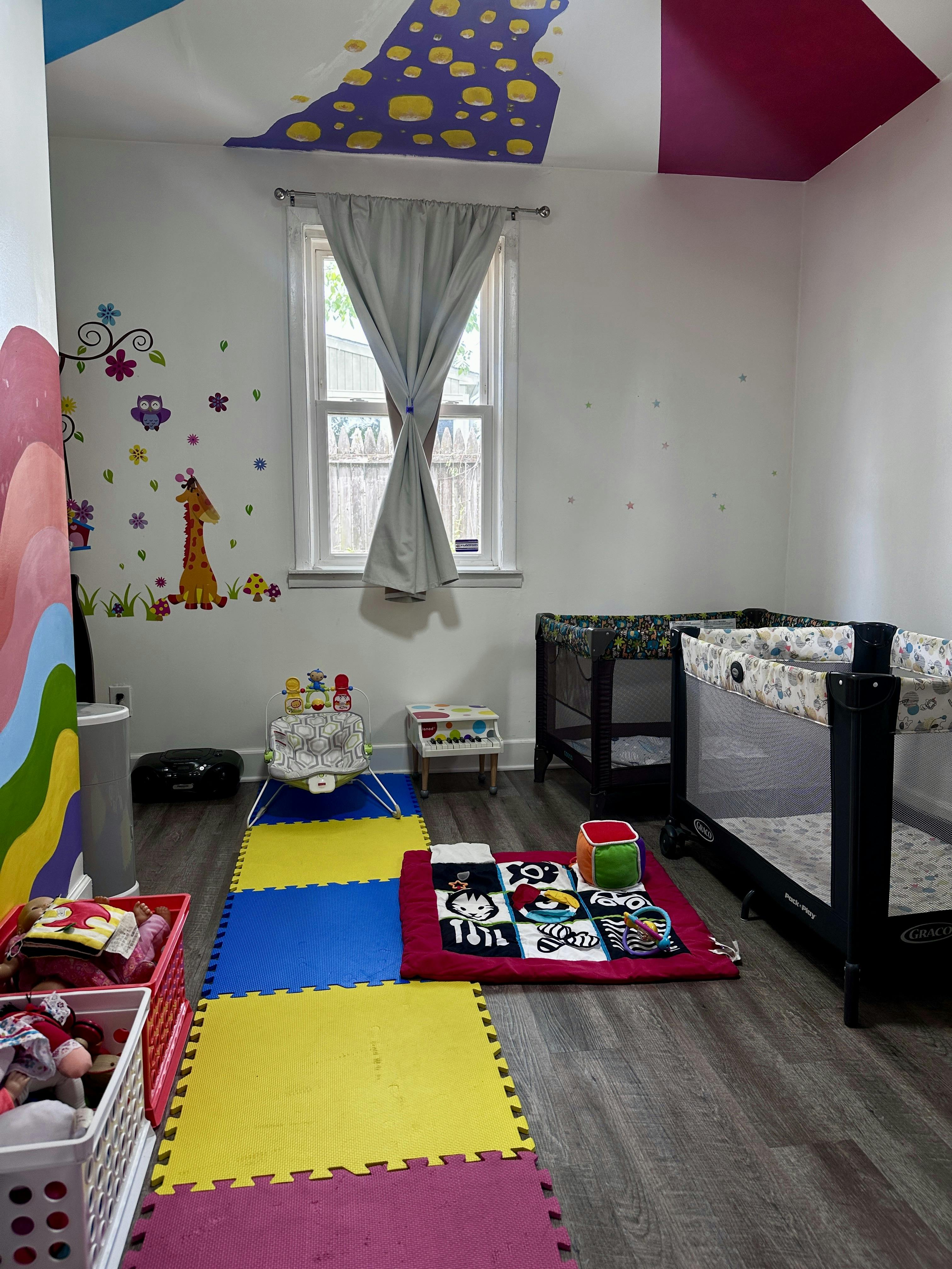 Baby room with play mats, two bassinets, and colorful wall decals