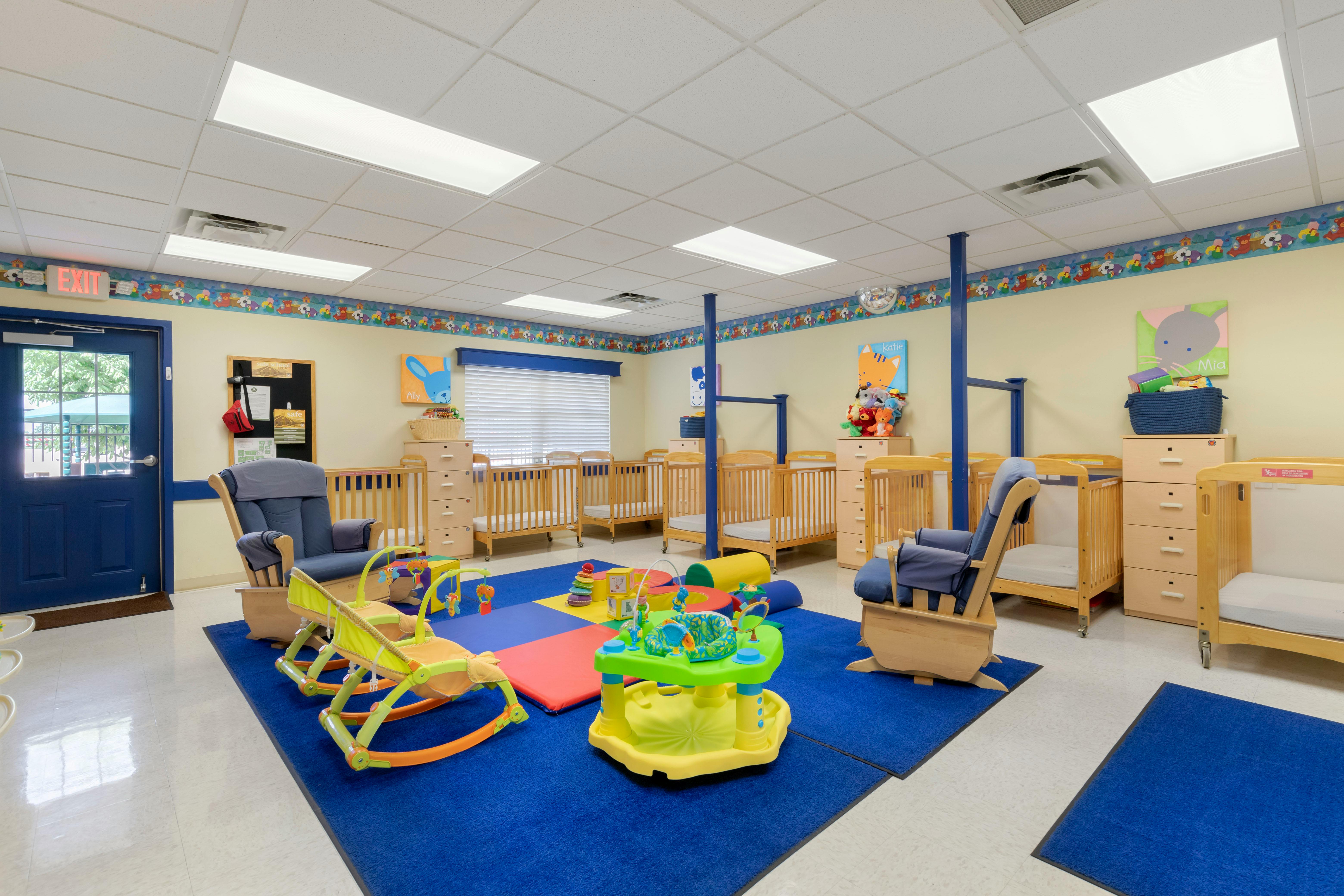 An empty nursery room with multiple cribs, rockers, and infant play items