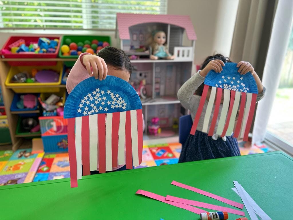 Two children holding up paper plate crafts resembling American flags