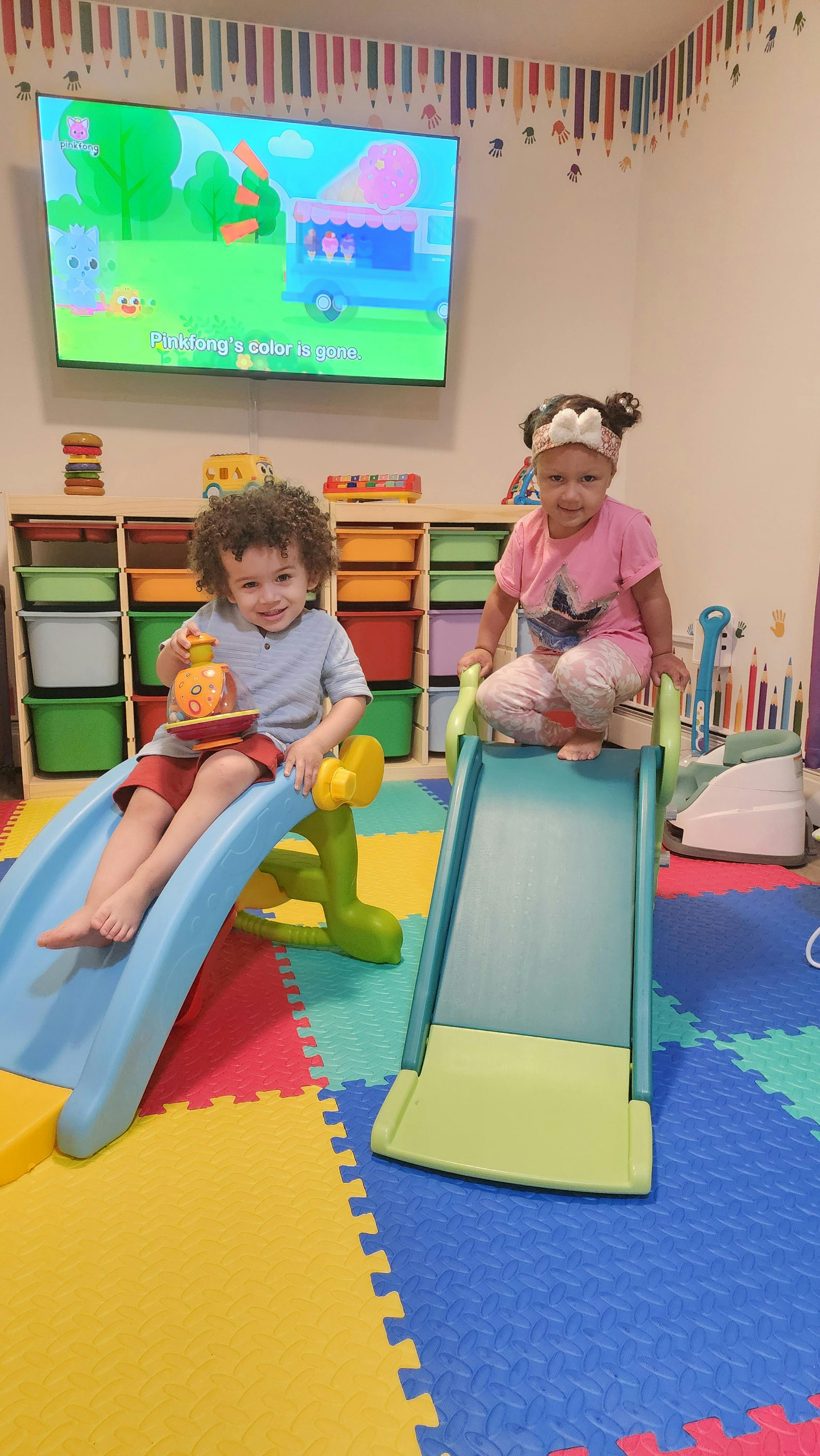 Two children sitting on small indoor slides in a playroom