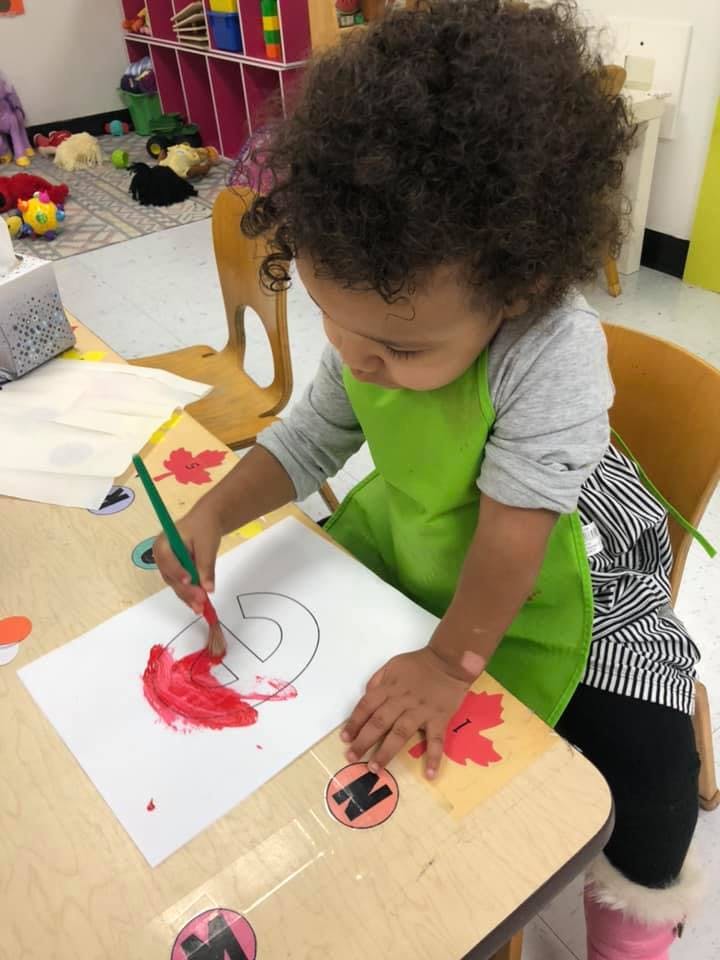 Child in a green apron painting a letter on paper at a table