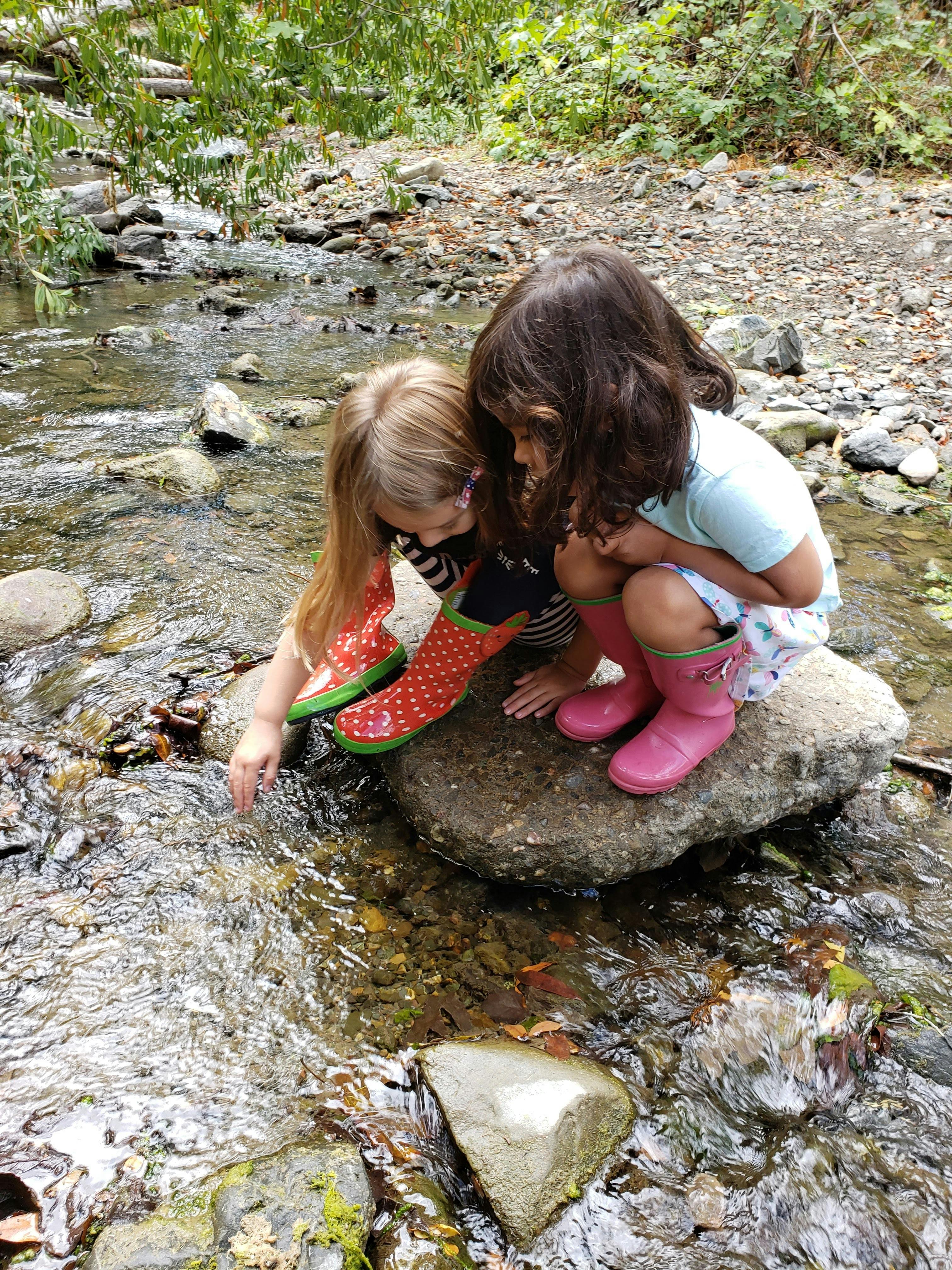 Two children in rain boots playing in a shallow stream