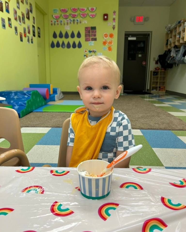 Child in a bib sitting at a table with a cup of food