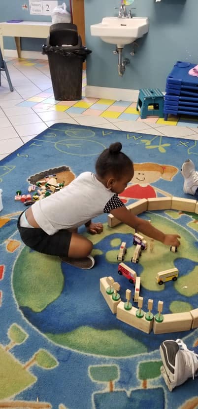 Child playing with wooden blocks and toy cars on a rug