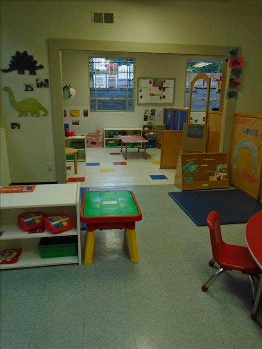 Classroom with small tables and chairs, and a doorway to another play area