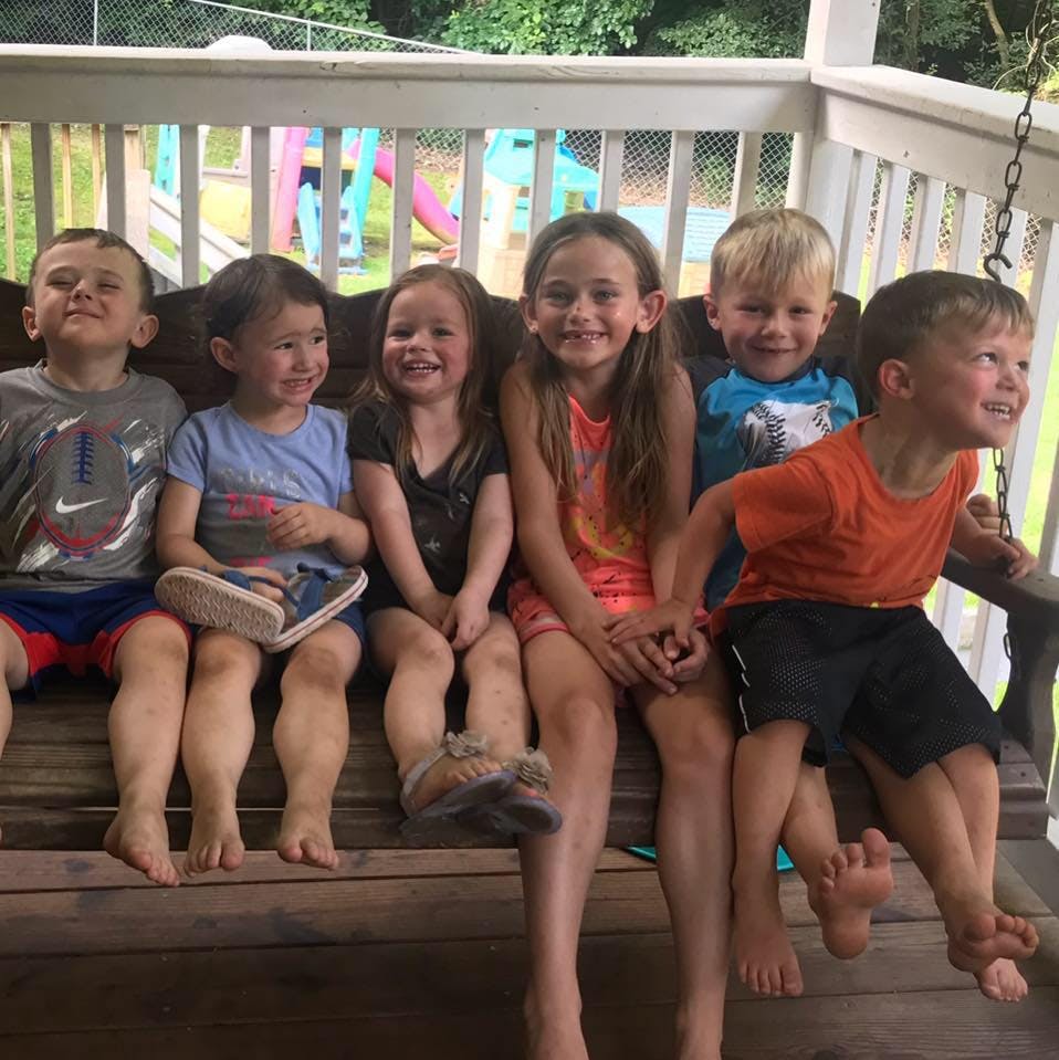 Five children and one teen sitting on a wooden porch swing