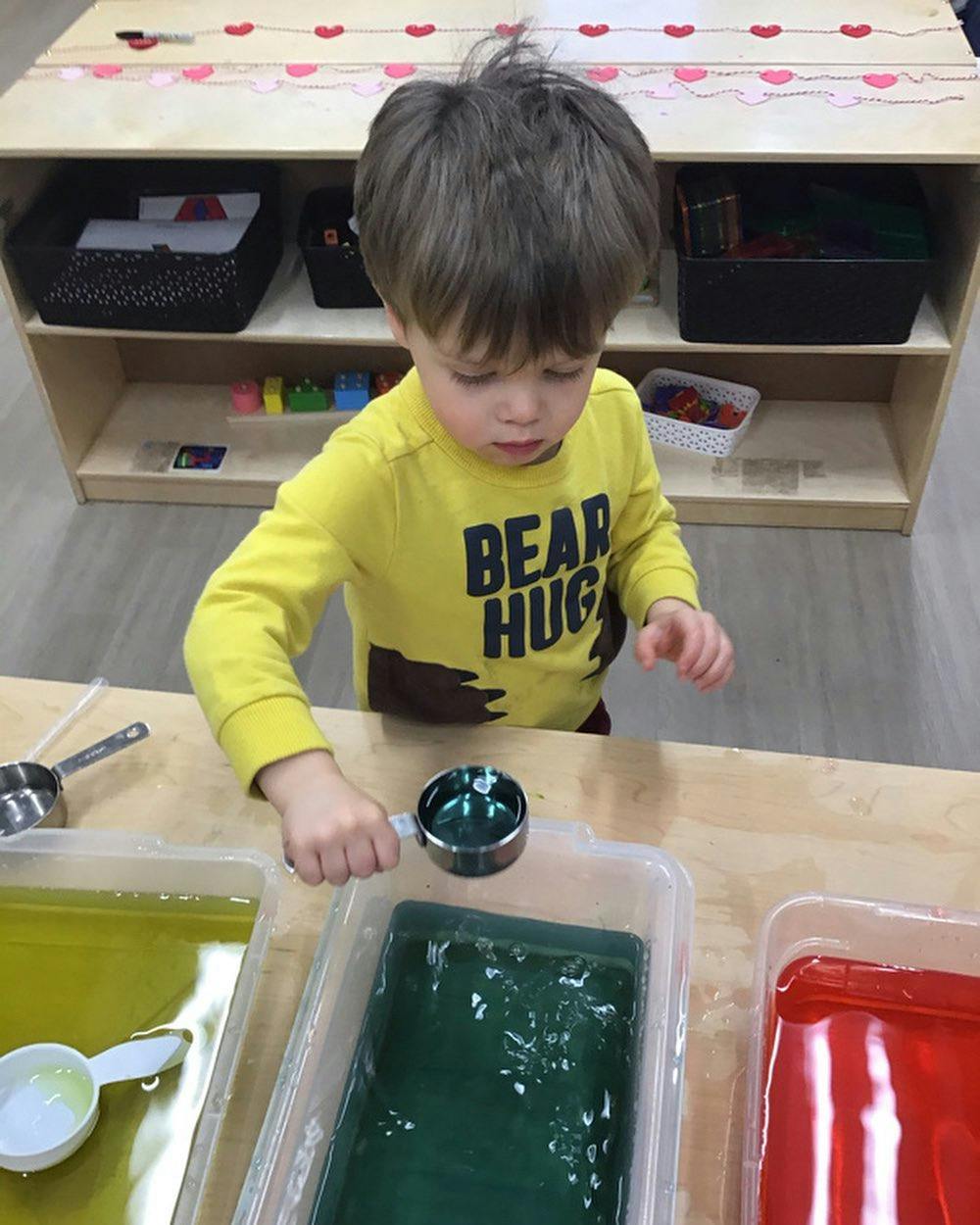 Child playing with colored liquid in clear bins